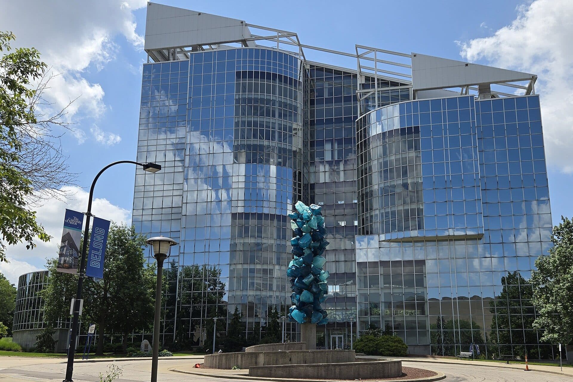 The twin glass towers of the Goodyear Polymer Center reflecting a blue sky, with a sculpture on a plaza in front, on the University of Akron campus