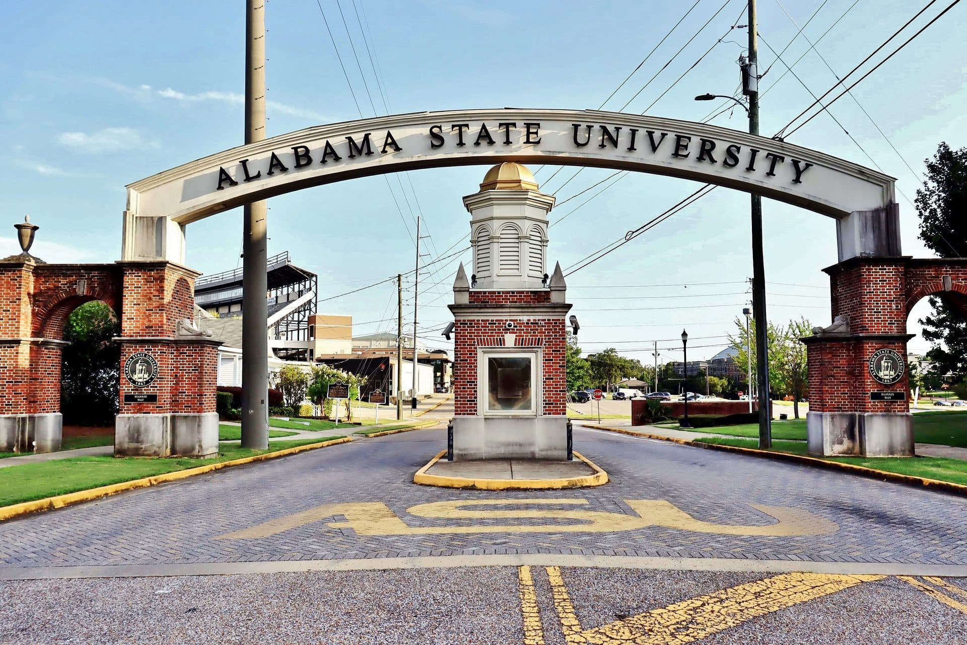 A brick and stone archway reading Alabama State University spanning a campus road under a blue sky