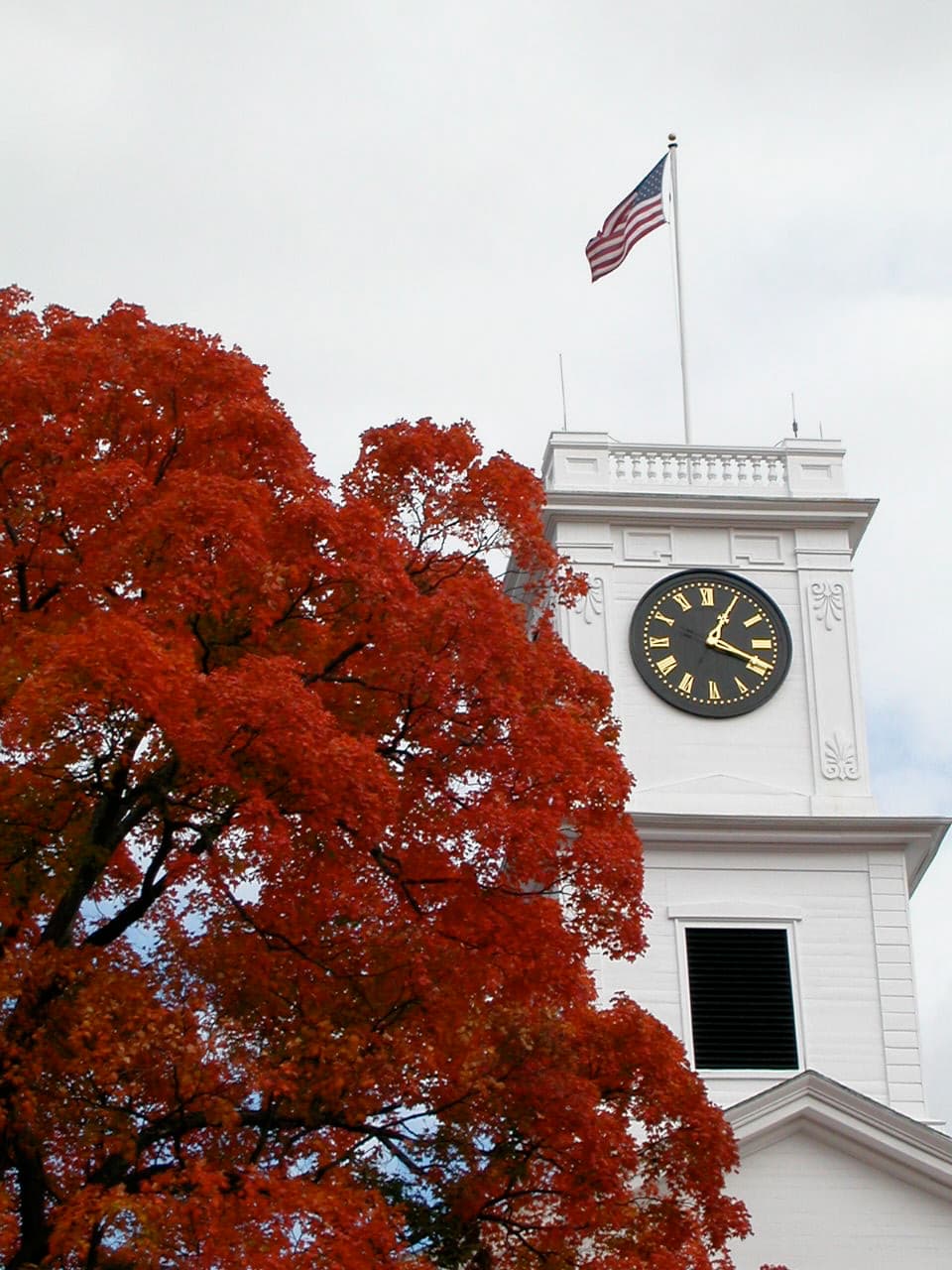 The white clock tower of Johnson Chapel at Amherst College beside a bright red autumn tree