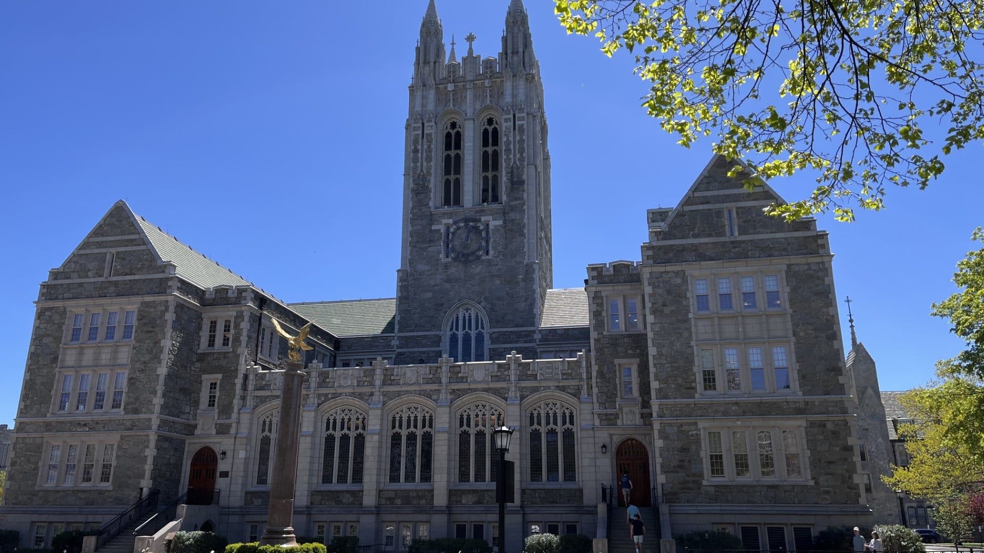 The Gothic stone tower of Gasson Hall at Boston College under a clear blue sky