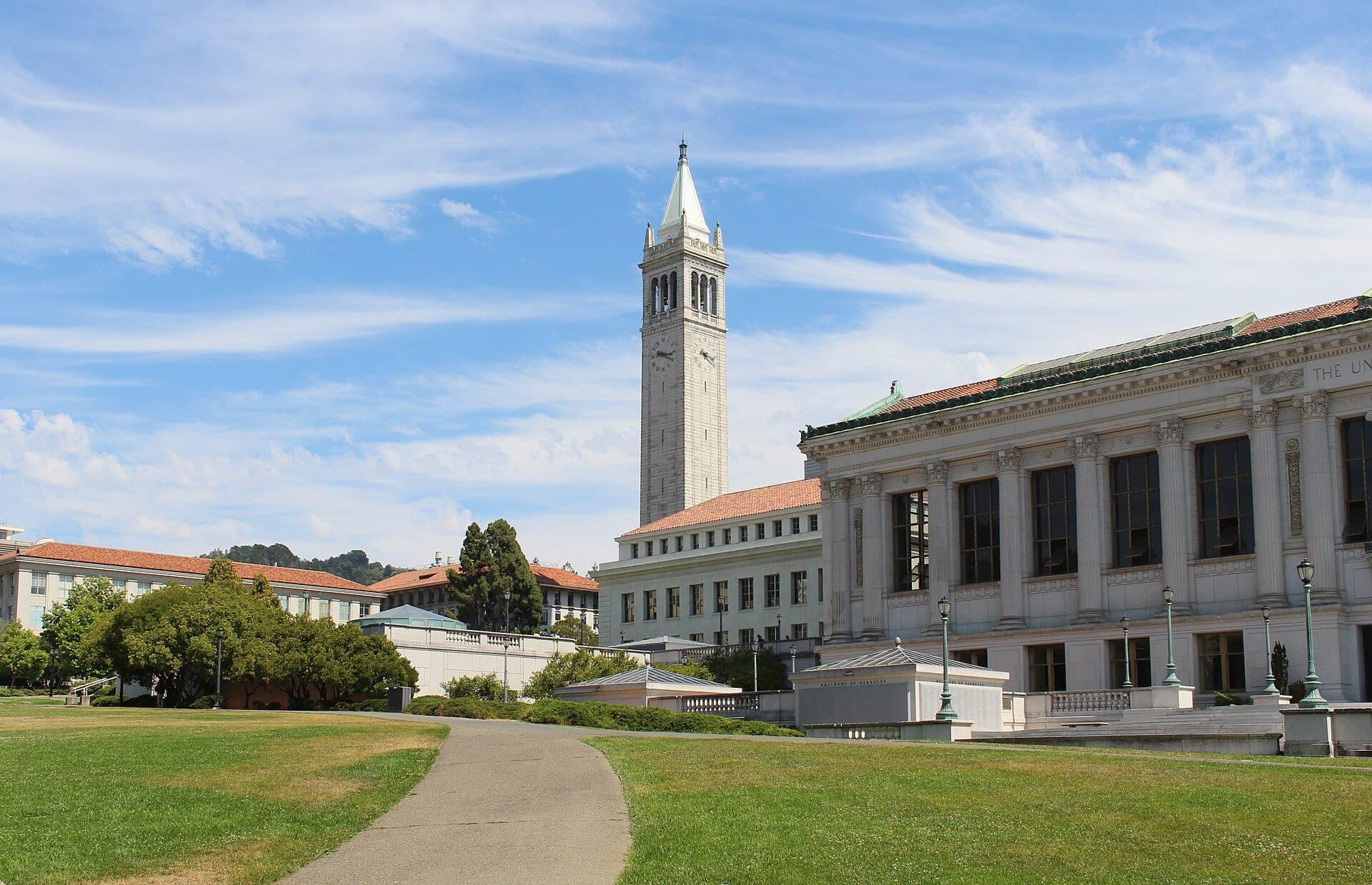 Sather Tower, UC Berkeley's white granite campanile, rising beyond a columned library and the green lawn of Memorial Glade on a sunny day