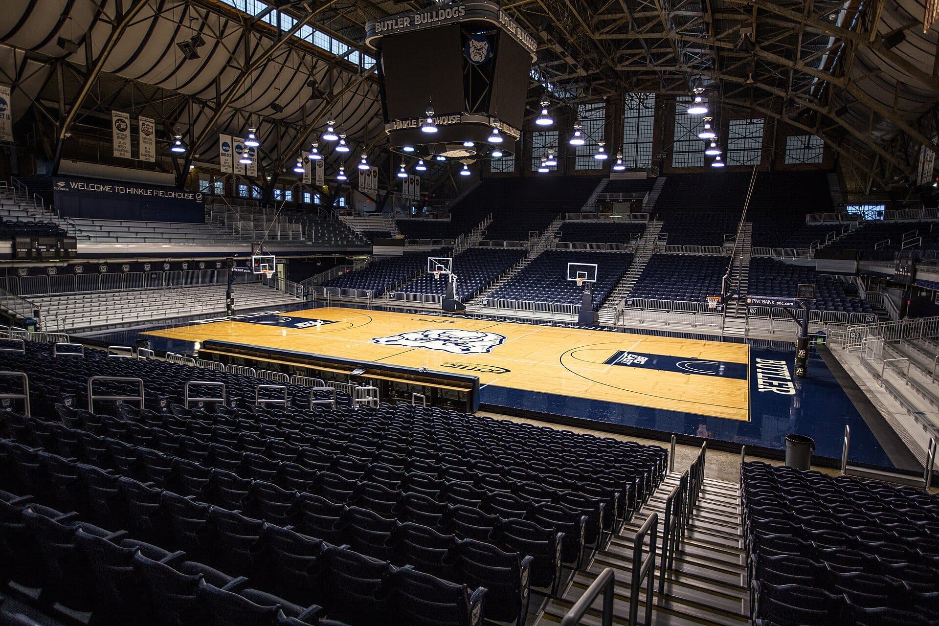Inside Butler's historic Hinkle Fieldhouse, rows of empty seats looking down on the basketball court under arched steel roof trusses