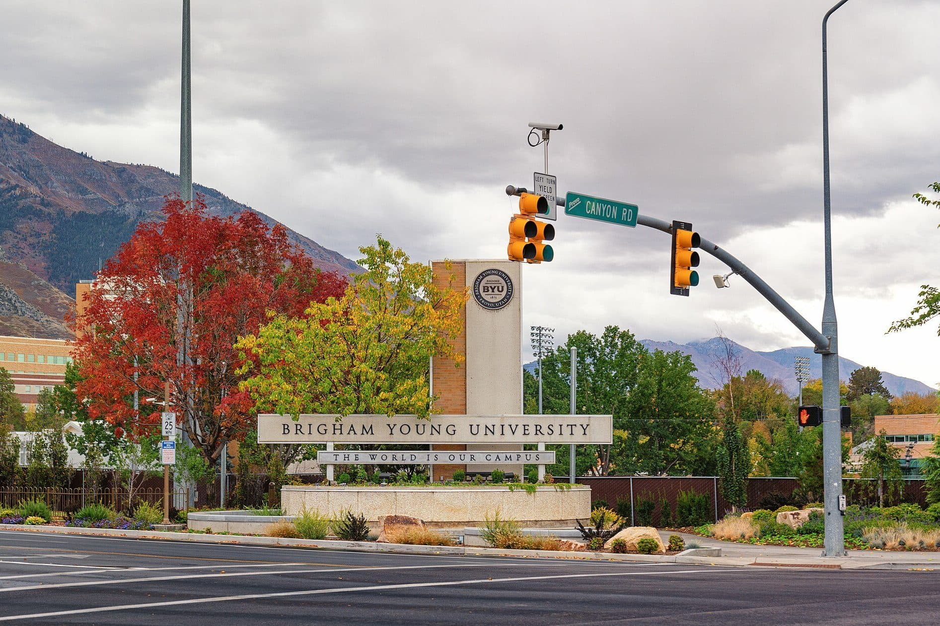 BYU's stone Brigham Young University entrance sign at a street corner, with red and gold autumn trees and mountains behind
