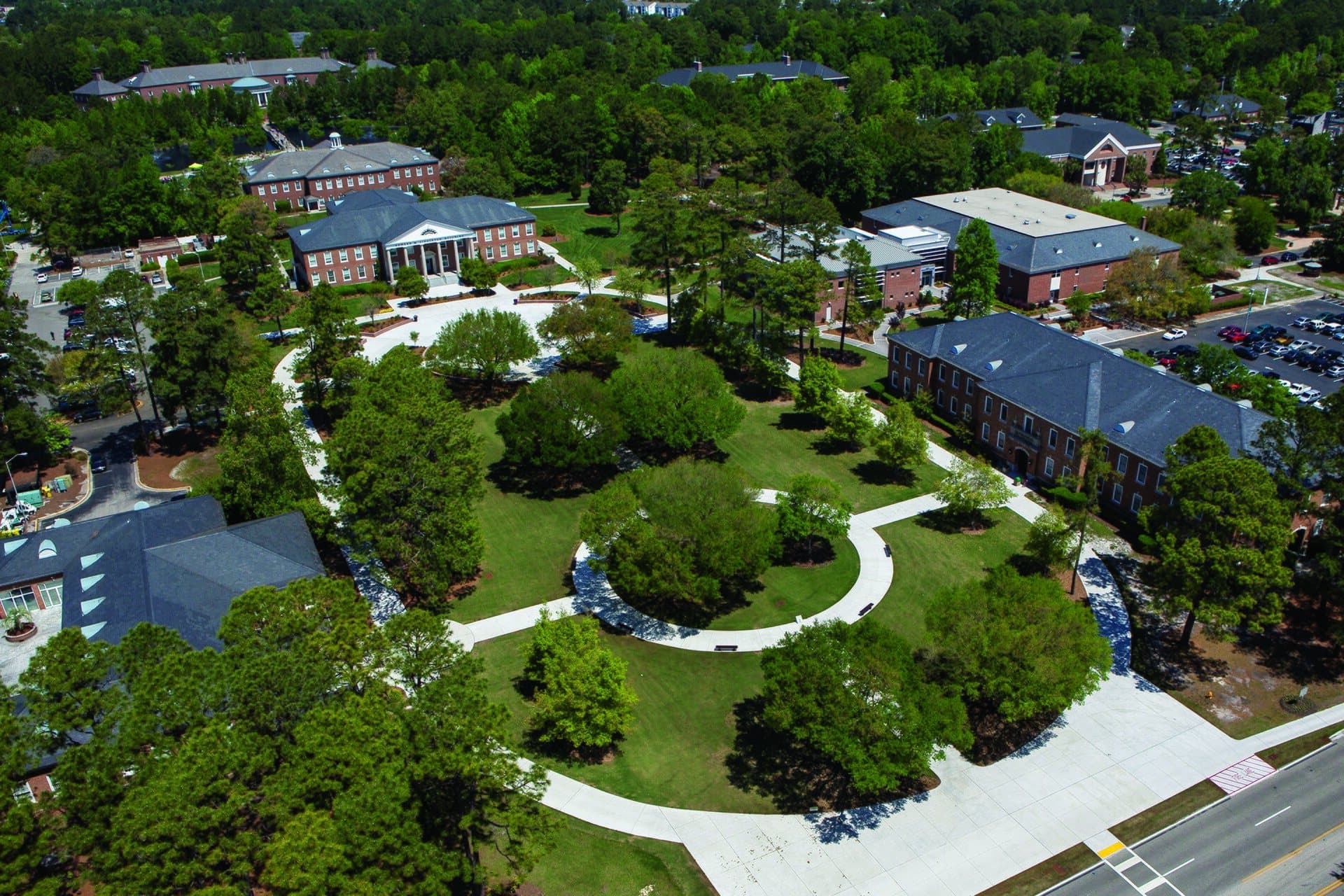 Aerial view of Blanton Park at Coastal Carolina University, a green lawn with curving paths and trees surrounded by red-brick buildings with gray roofs