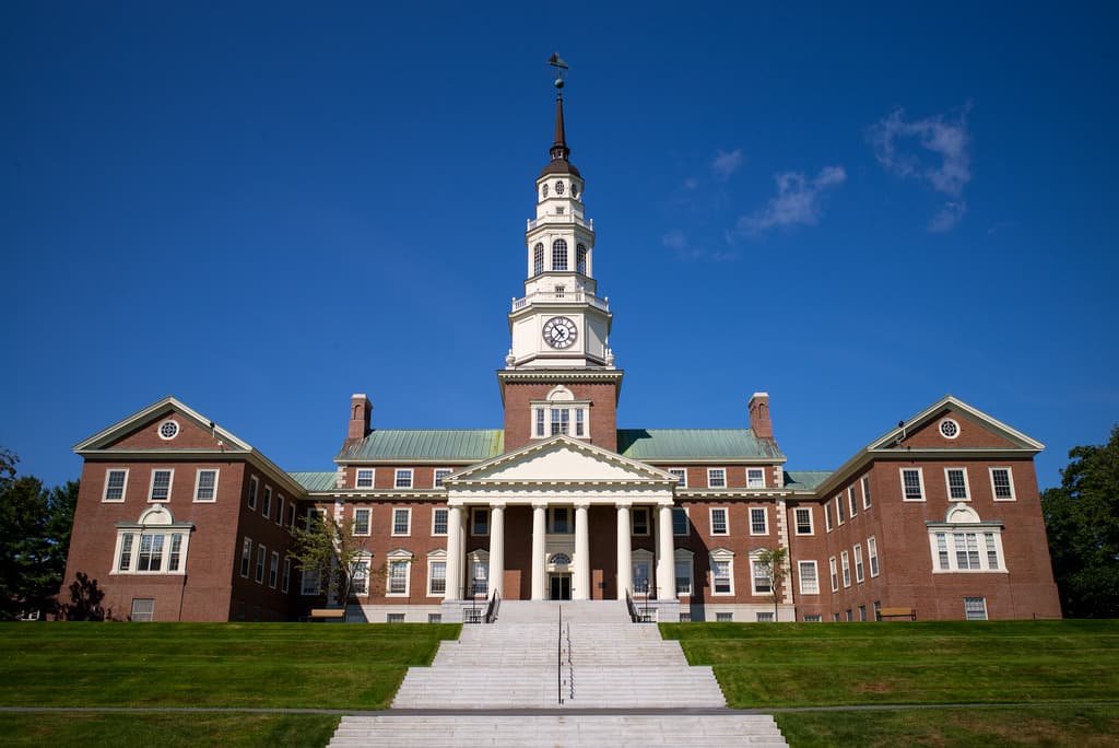 Colby's red-brick Miller Library with a white columned portico and a tall white clock tower, above wide steps and a lawn under a blue sky