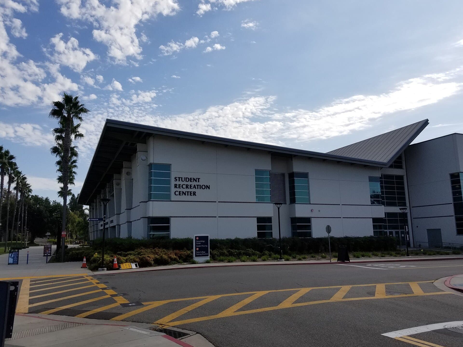 Cal State Fullerton's Student Recreation Center, a modern white and gray building with its name on the front, palm trees and a parking lot