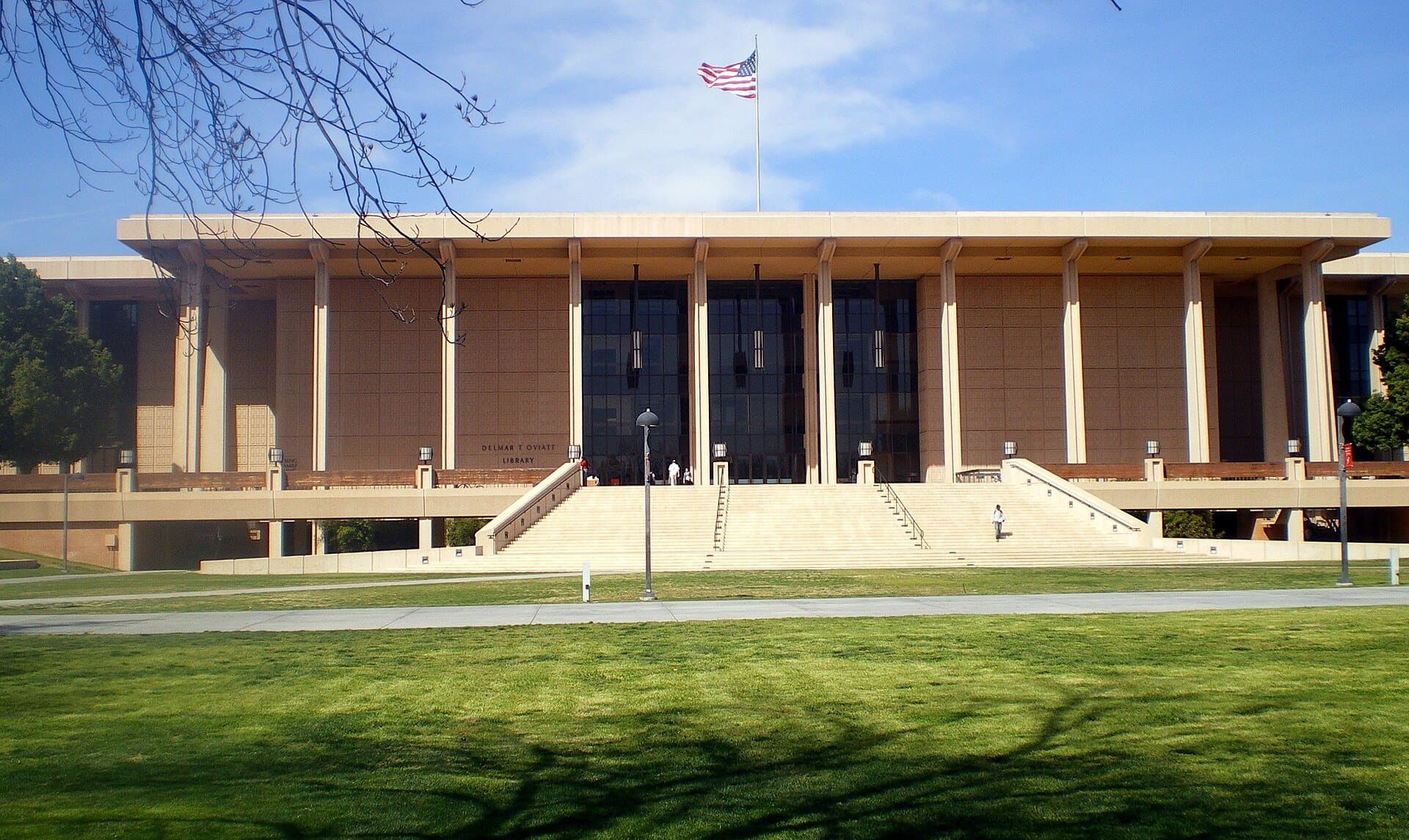 The Oviatt Library at Cal State Northridge, a long building with a columned facade behind a wide green lawn, with a flag flying