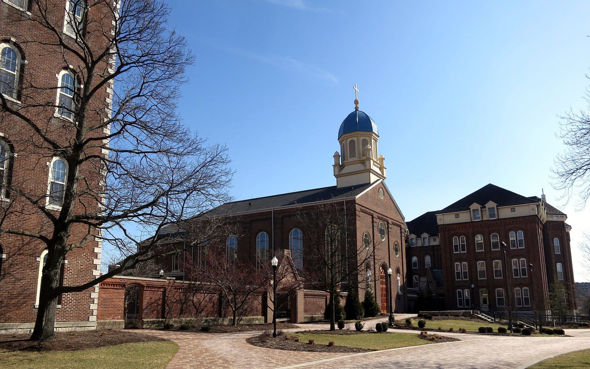 The brick Chapel of the Immaculate Conception at the University of Dayton, with its blue dome and gold cross, beside a brick building under a clear sky