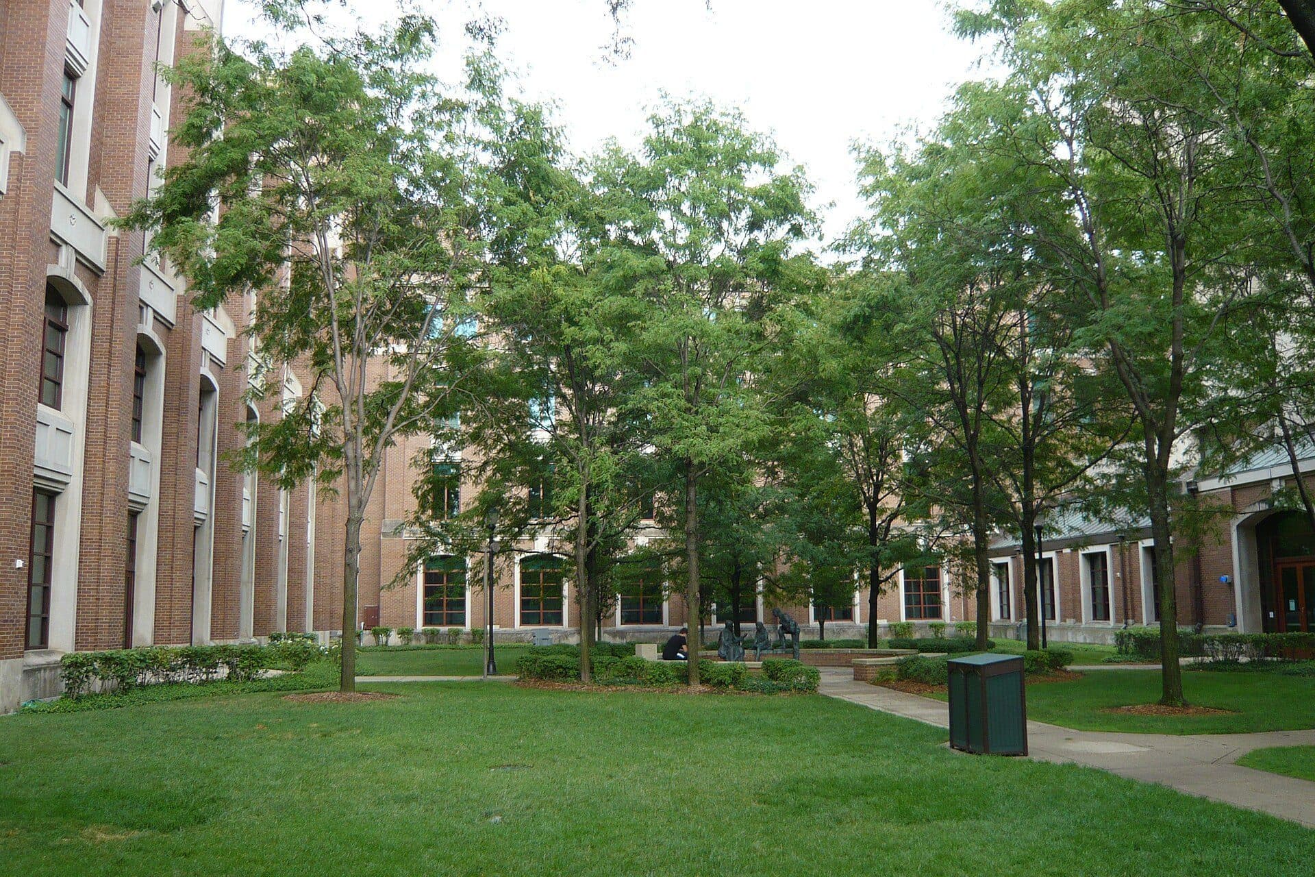 A green lawn shaded by leafy trees between red-brick buildings on DePaul's Lincoln Park Campus