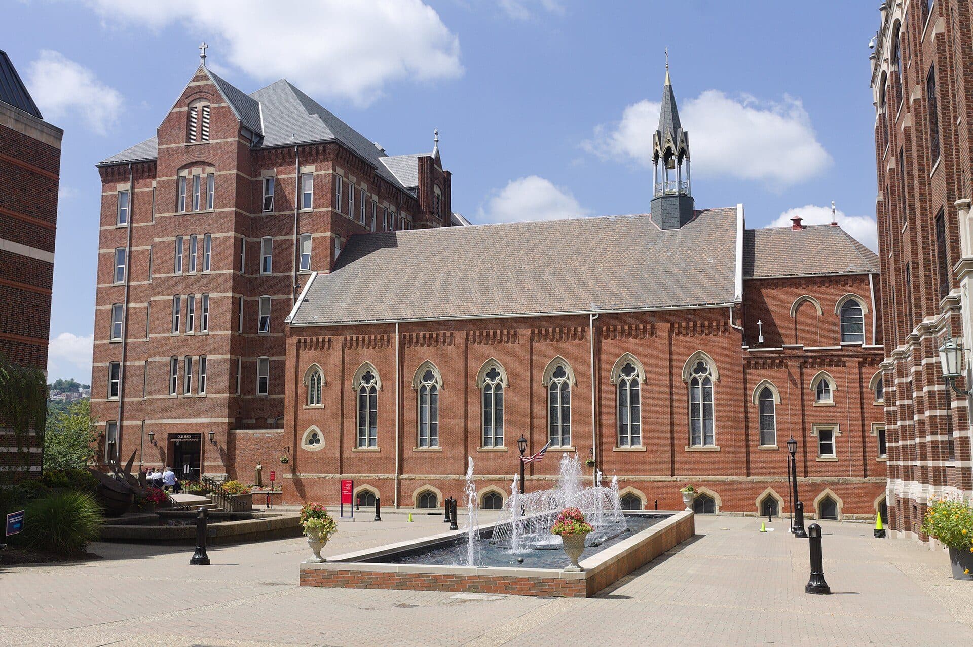 A fountain on Duquesne's Academic Walk in front of the red-brick Chapel of the Holy Spirit and Old Main under a blue sky