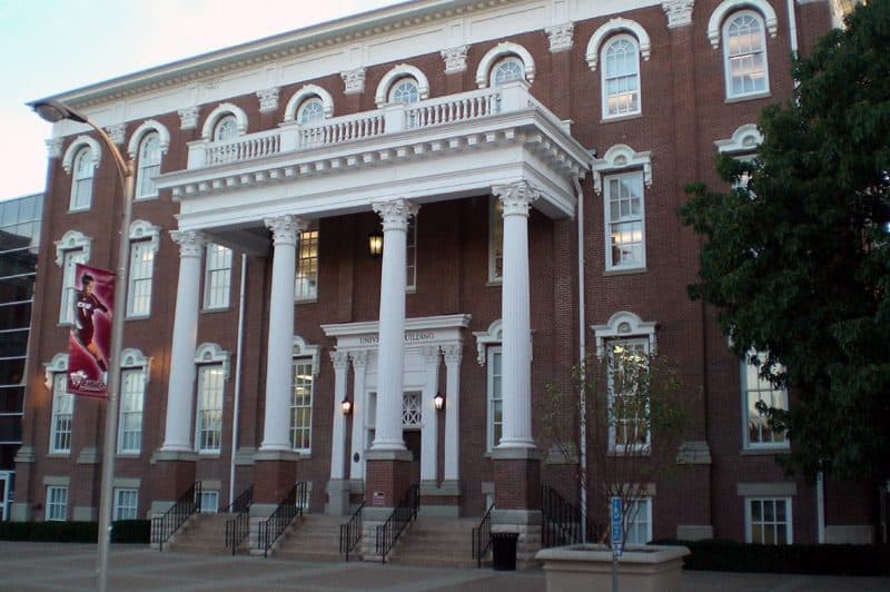 The red-brick University Building at EKU with a white columned portico, arched windows and a maroon banner out front