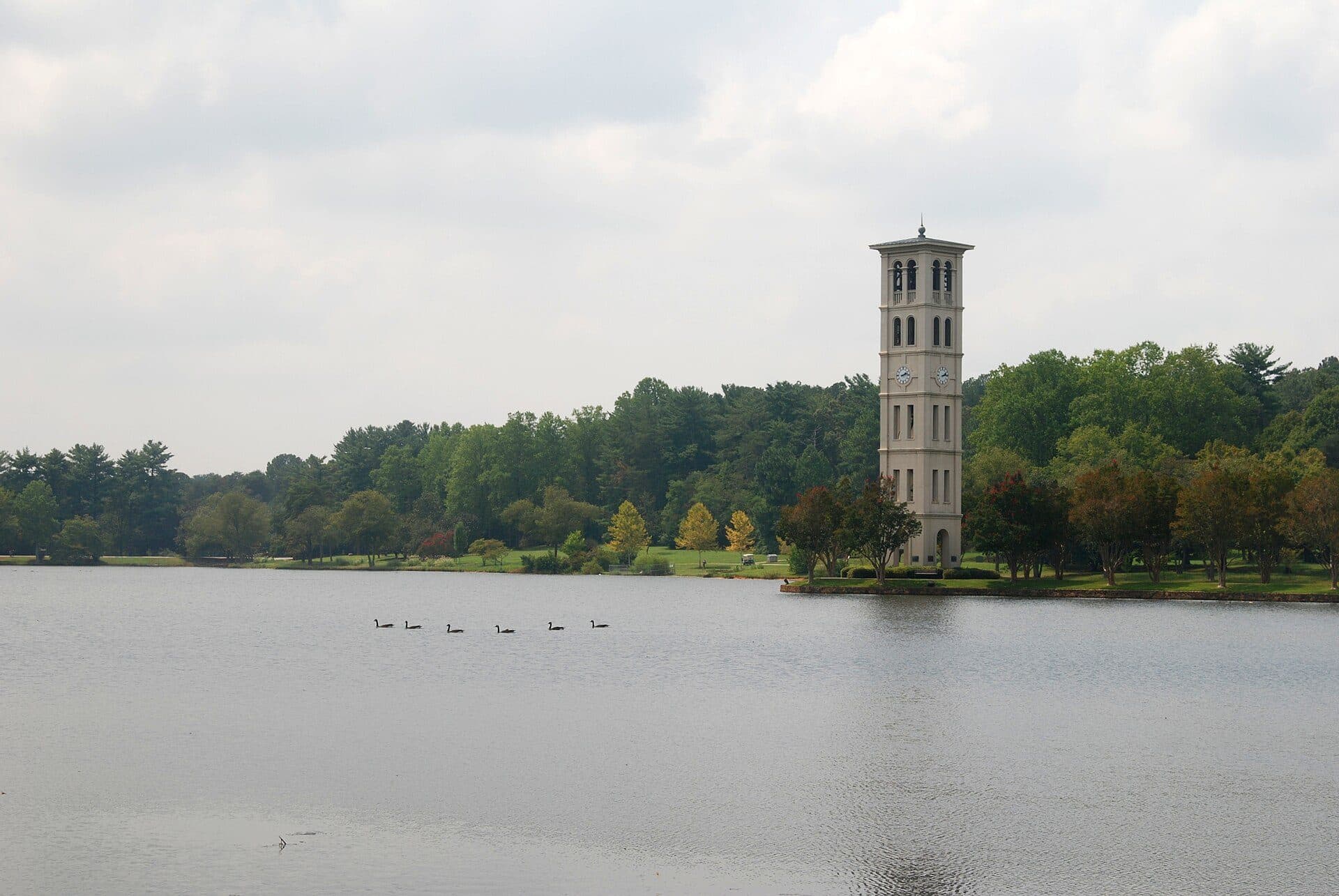 Furman University's stone Bell Tower on the far shore of Furman Lake, with geese on the water and green trees behind