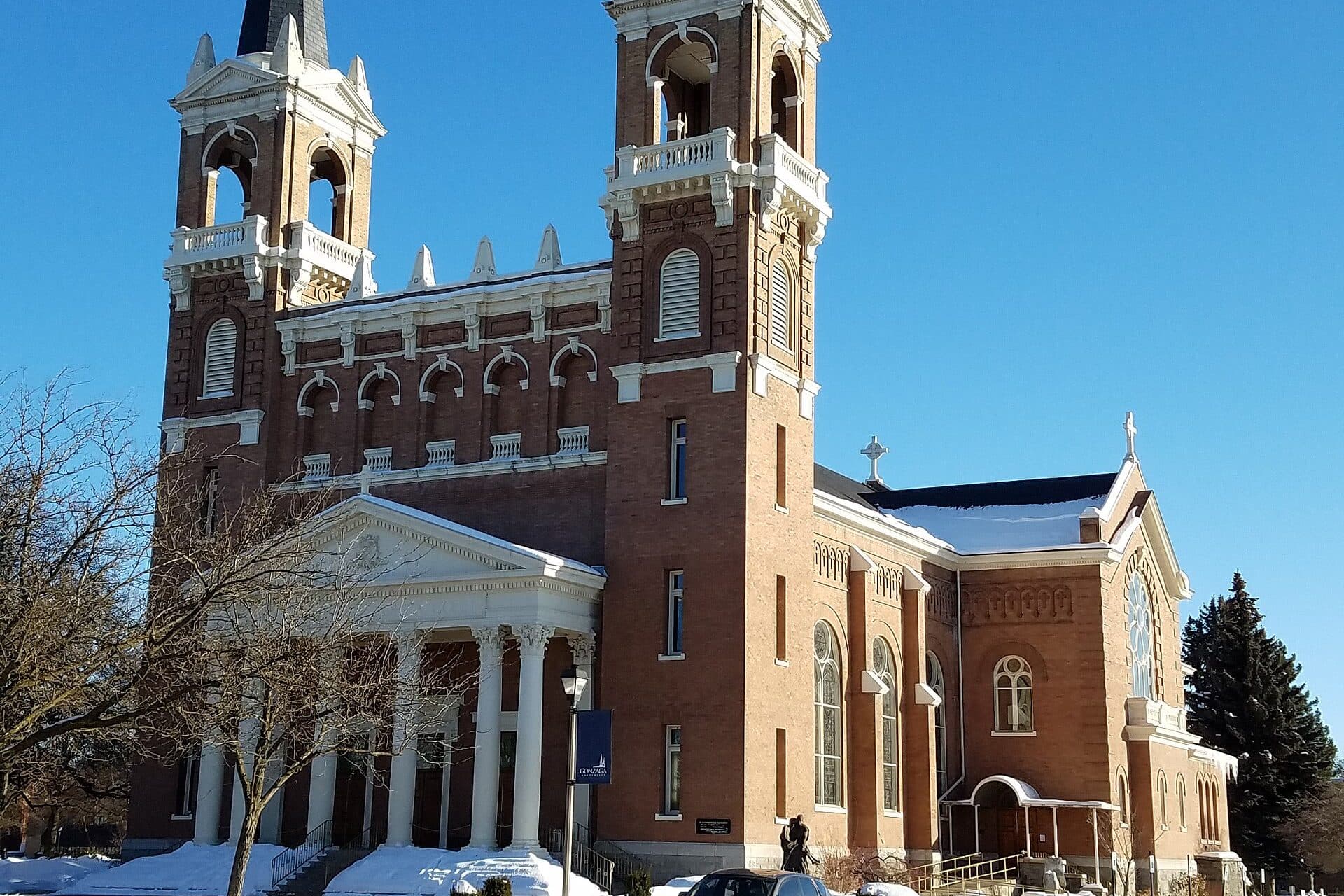 St. Aloysius Church's twin white-trimmed brick spires and columned entrance against a deep blue sky, with snow at the base