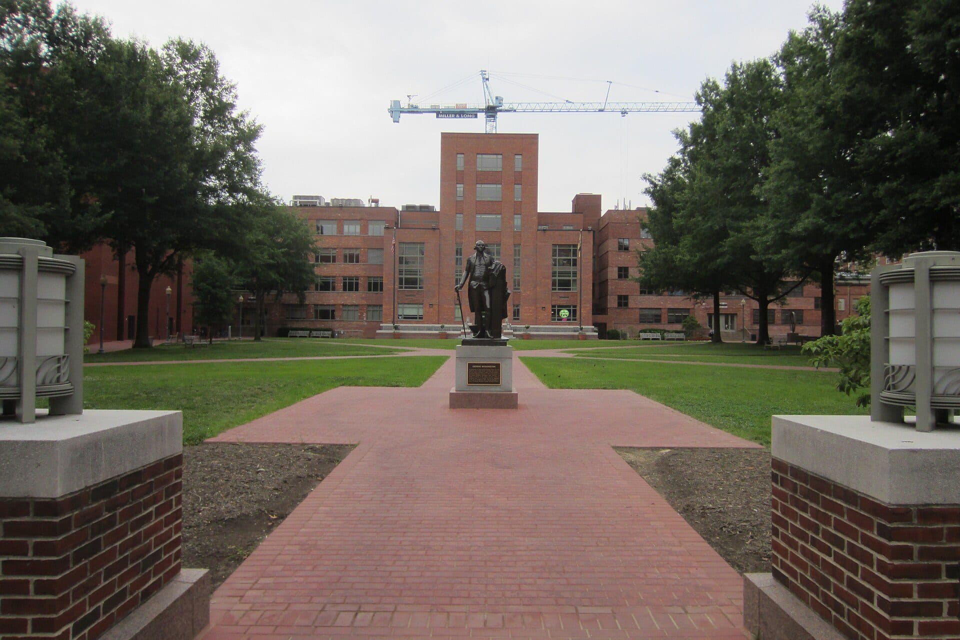 A brick path through University Yard at George Washington University, leading past lawns to a statue of George Washington and brick buildings beyond