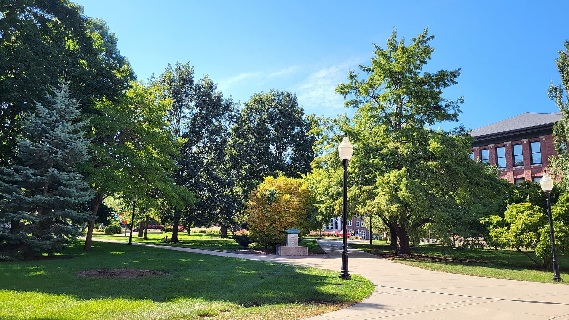 The tree-lined Quad at Illinois State University in late summer, with a wide lawn, walkways and a campus building beyond the trees
