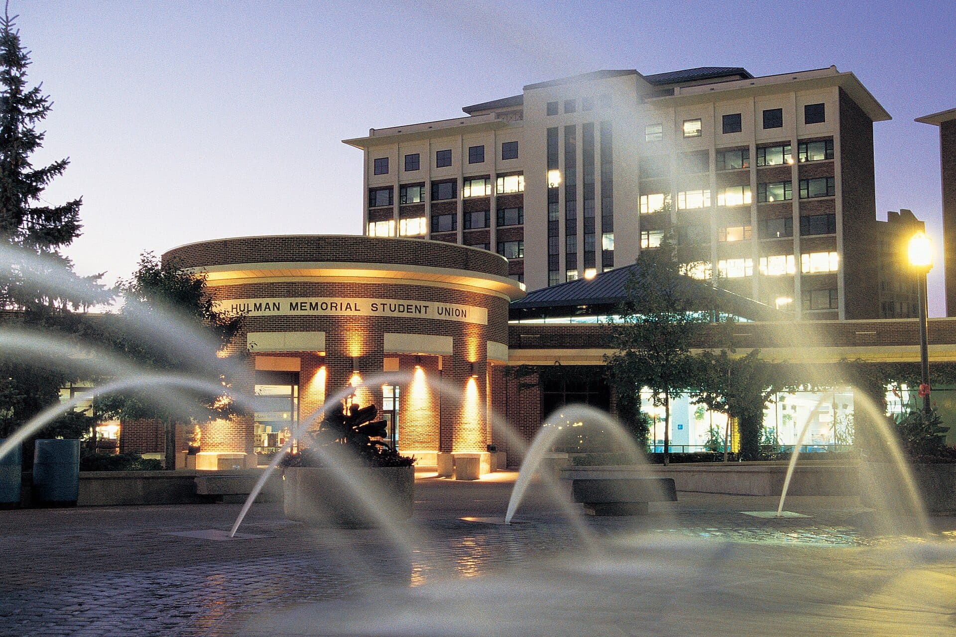 Fountains spraying in Dede Plaza at dusk, in front of the lit-up Hulman Memorial Student Union at Indiana State University