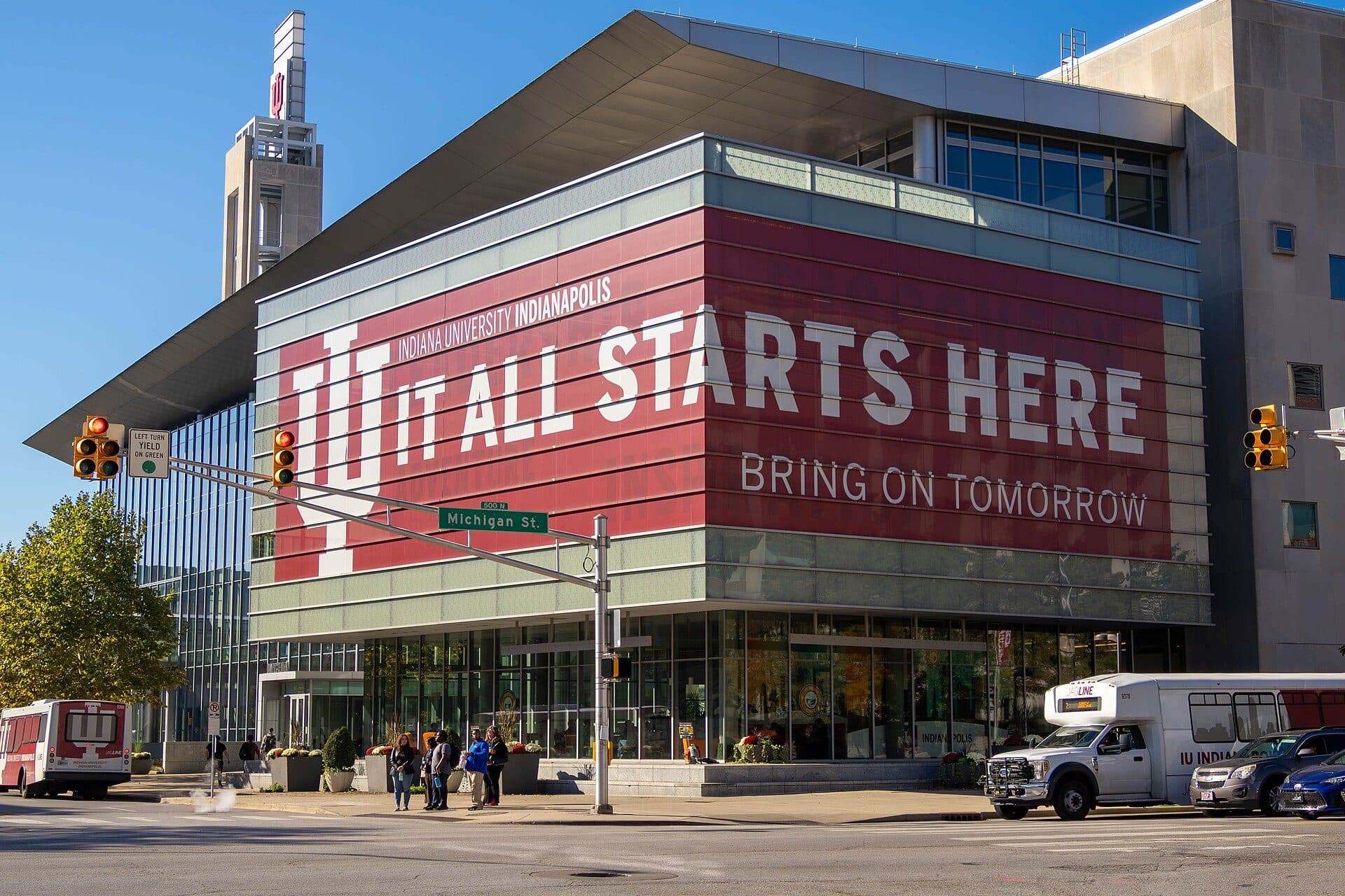 The glass-fronted Campus Center at IU Indianapolis with a large red banner reading It All Starts Here, Bring on Tomorrow, on a sunny day
