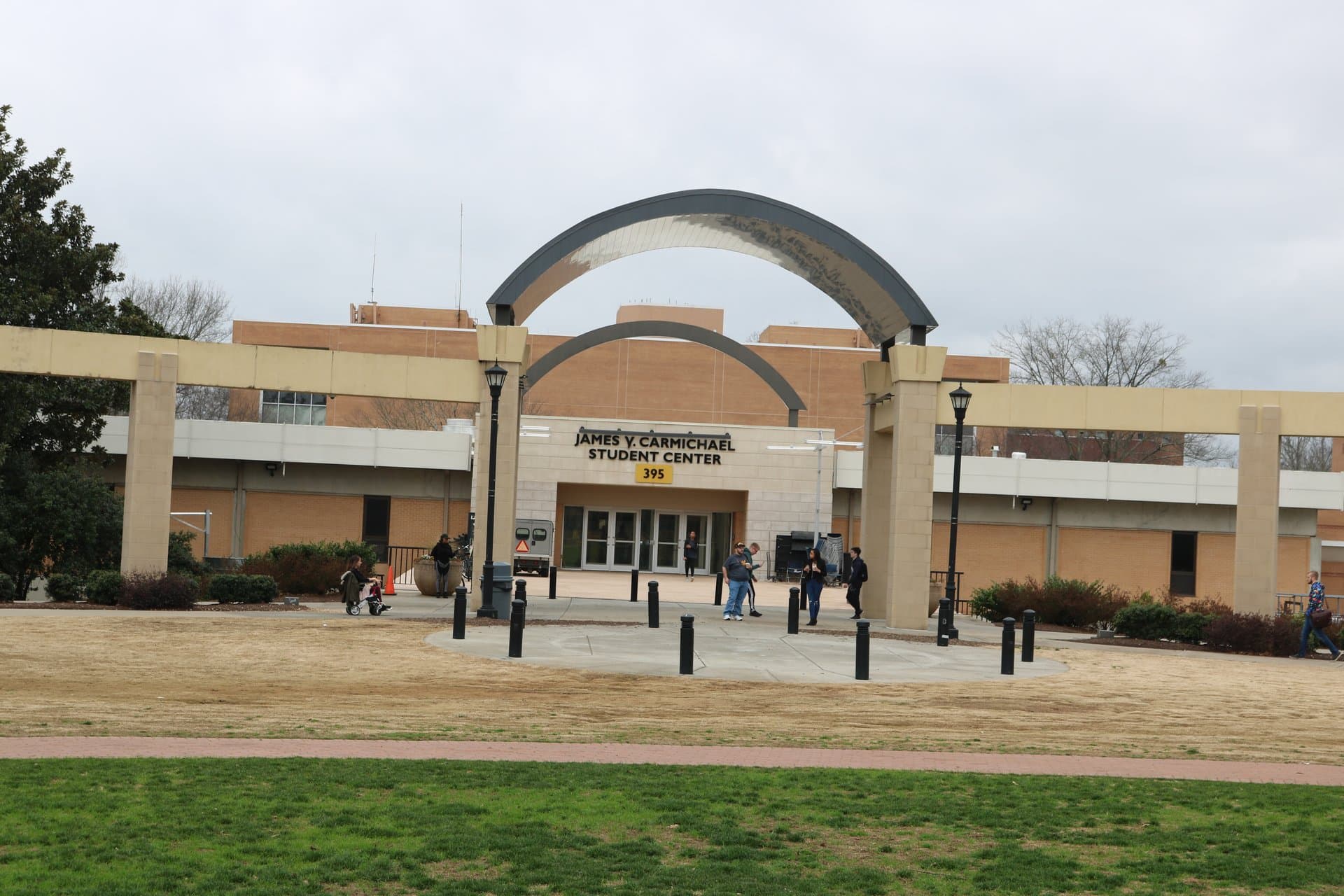 The James V. Carmichael Student Center at Kennesaw State, a tan brick building behind a pair of large curved arches and stone columns, with students walking on the plaza and a lawn in front