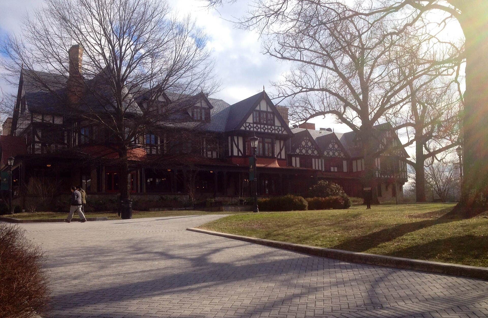Loyola Maryland's Humanities Center, a large Tudor-style building with half-timbered gables and red trim, behind a curving brick walk and lawn with tall bare trees in winter sun