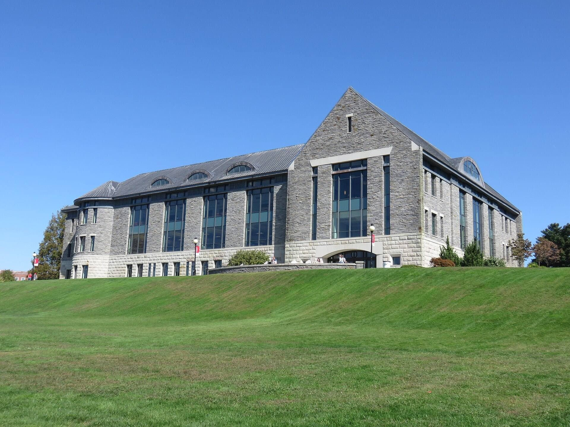 A large gray stone building with a slate roof at Marist University, above a grassy slope under a blue sky