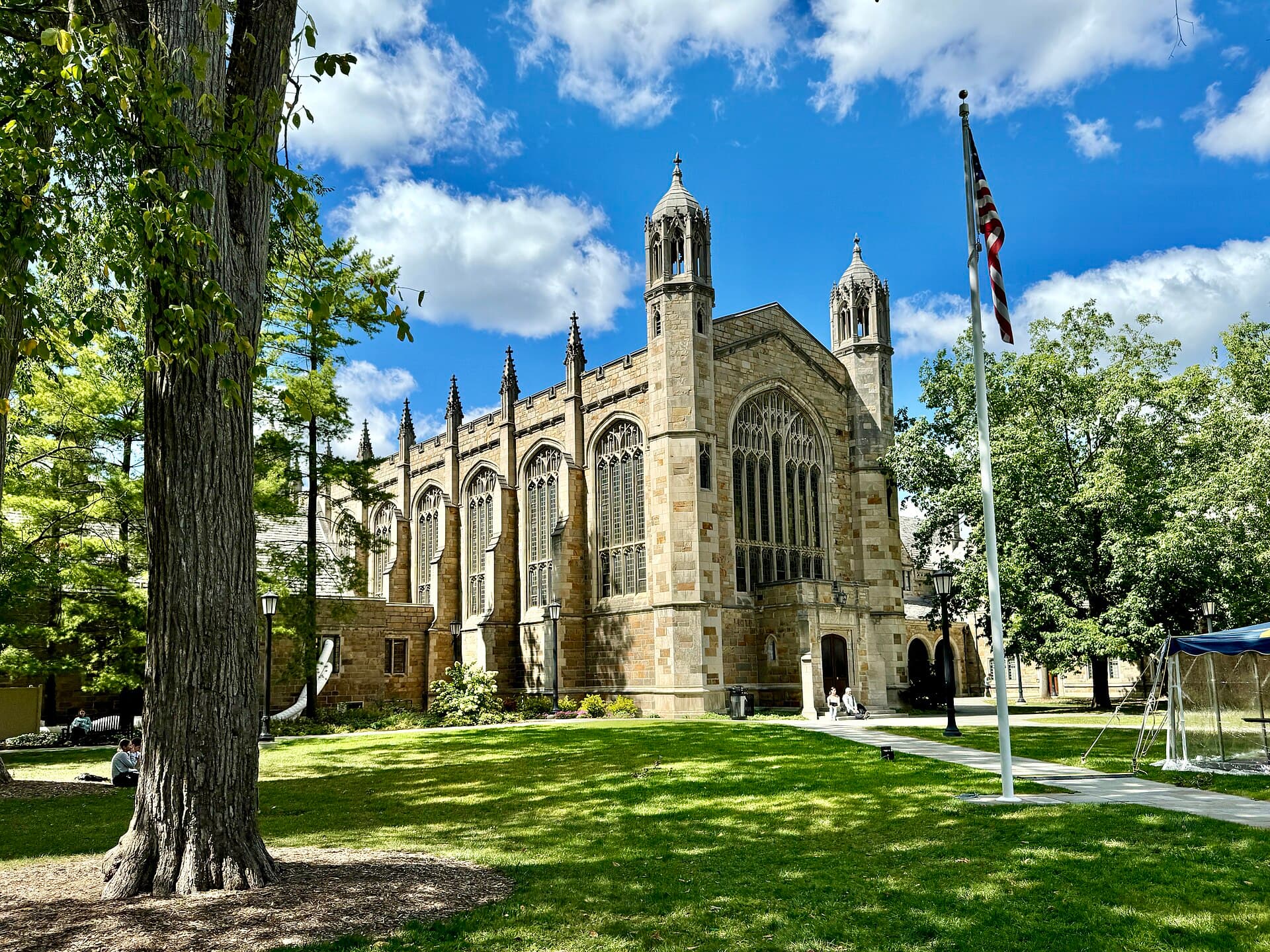 The Law Quadrangle's Gothic stone buildings with towers behind a sunny lawn and tall trees, with a flagpole