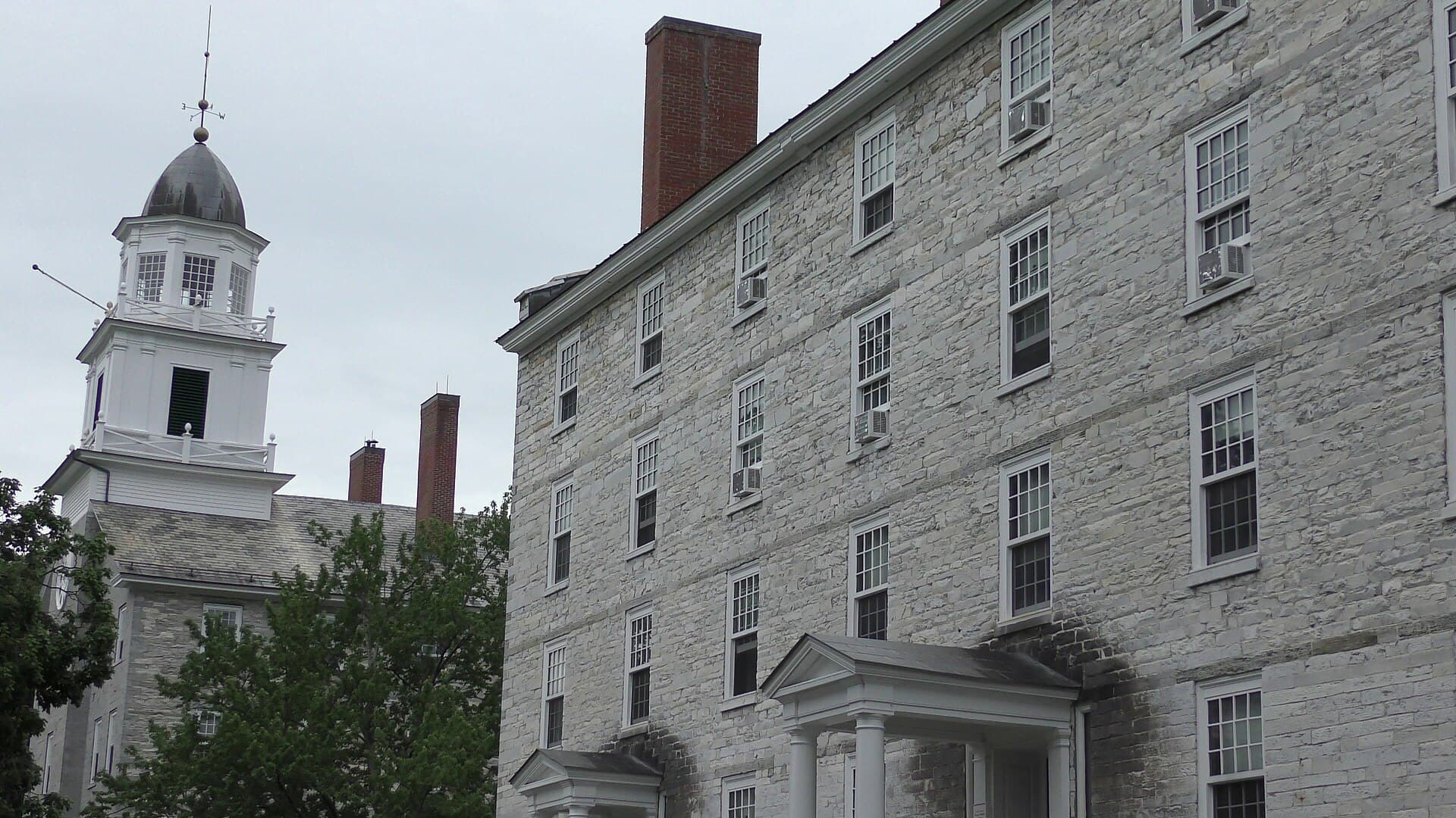 Middlebury's Old Chapel with its white cupola beside Painter Hall, a tall gray stone building, framed by trees