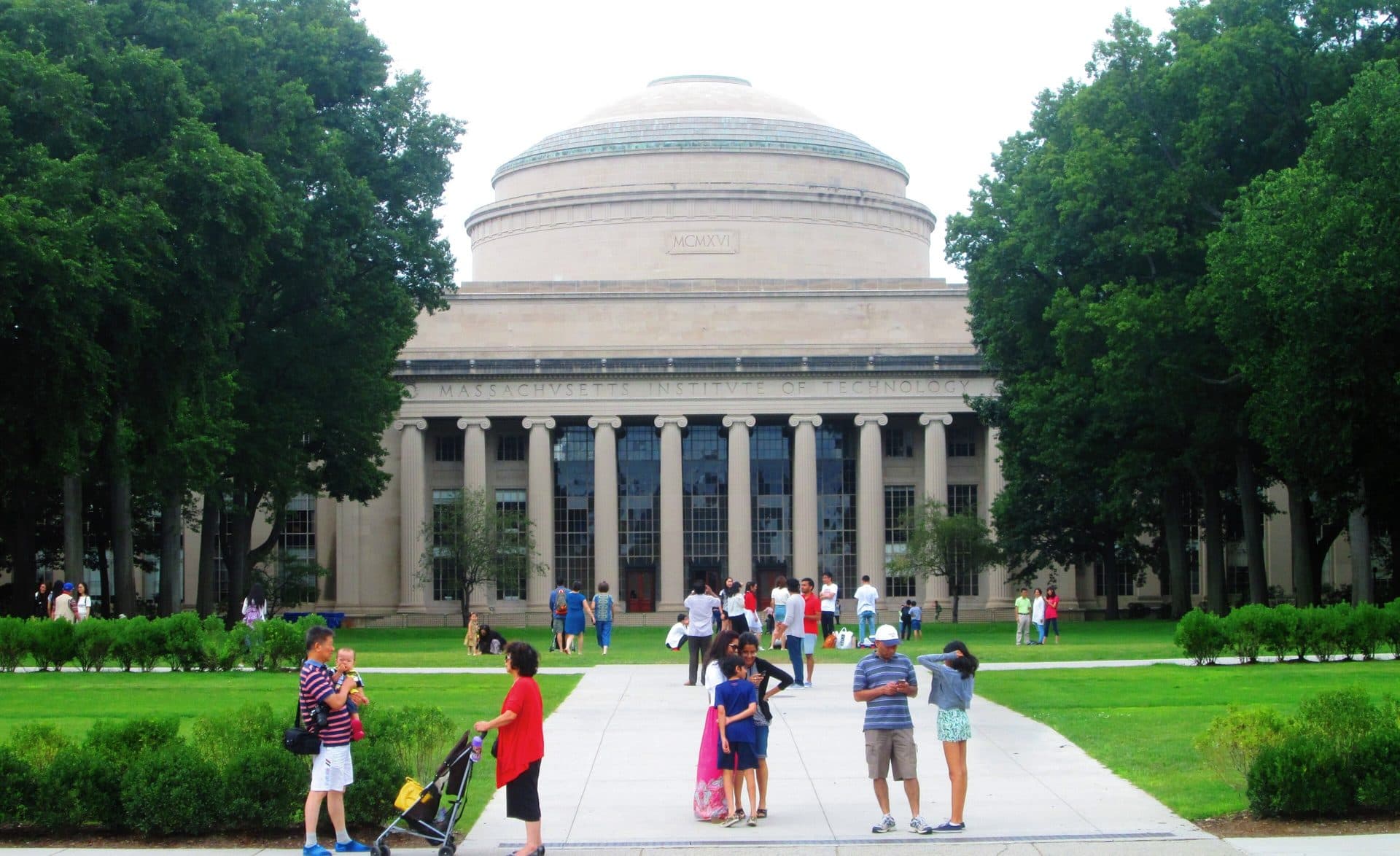MIT's Great Dome rising above the columned Maclaurin Buildings, with visitors walking along the path across the lawn in front