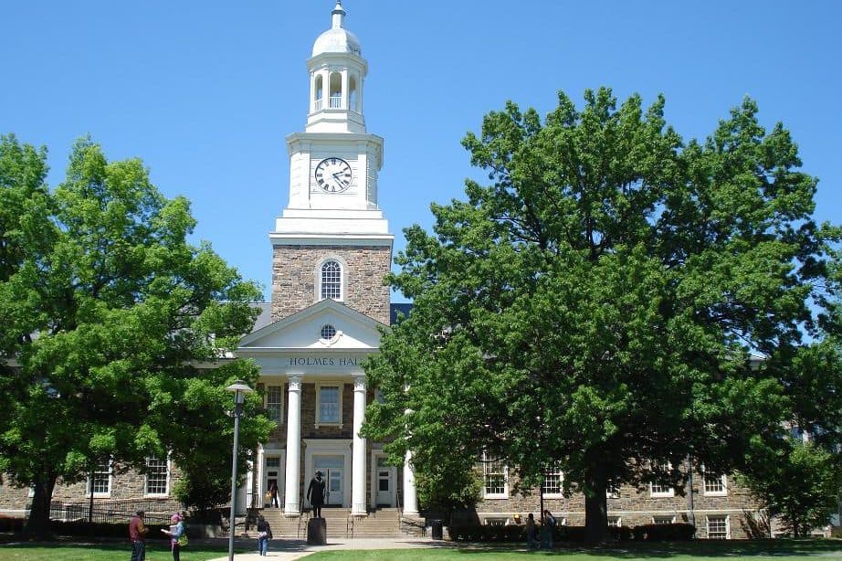 A white clock cupola above a columned stone hall framed by trees