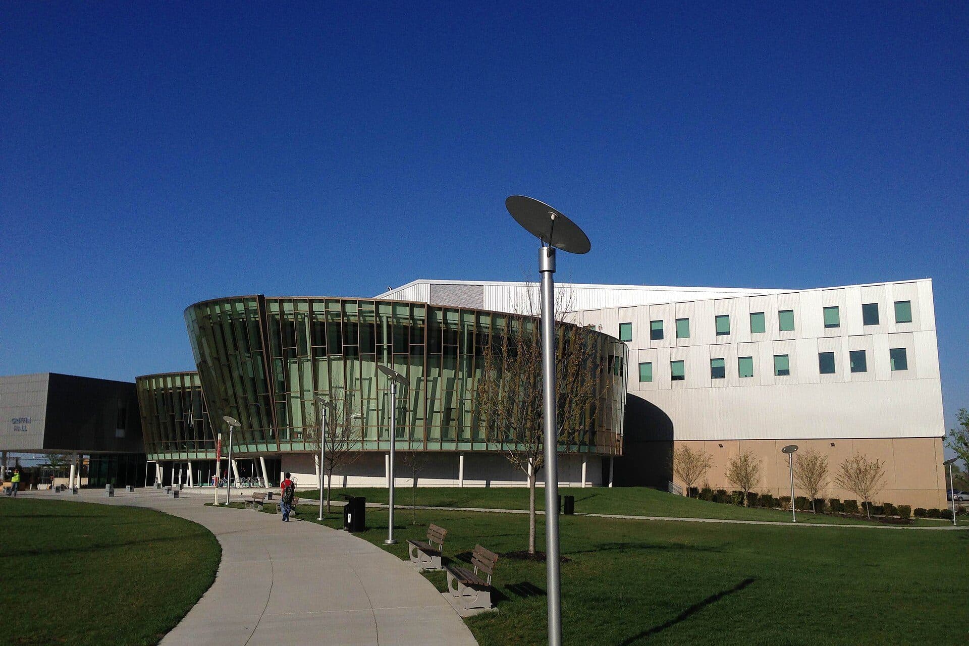 The glass-fronted Griffin Hall at Northern Kentucky University, curving beside a lawn and walkway under a deep blue sky