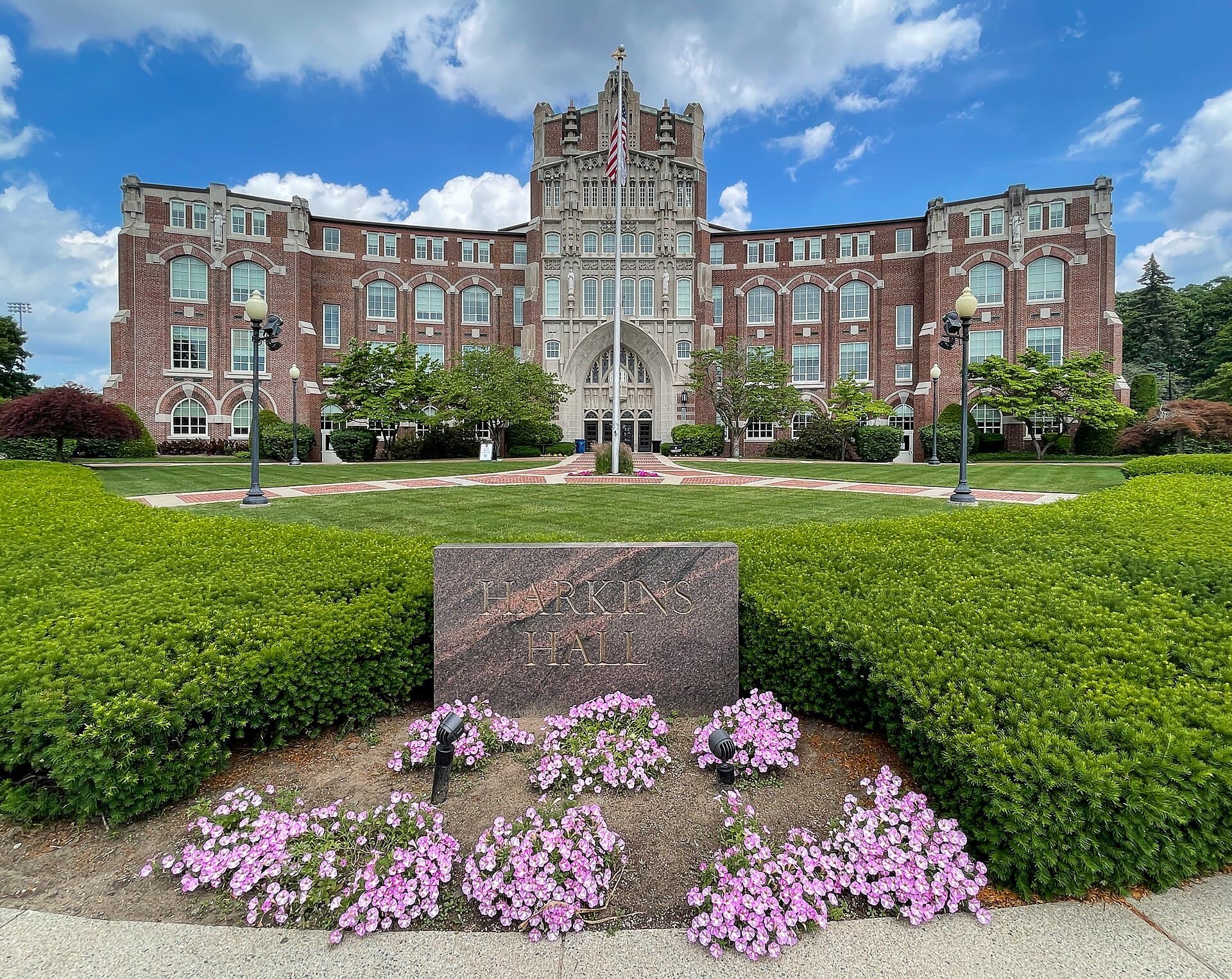 Harkins Hall at Providence College, a brick building with a central stone tower, behind a hedge and a flower bed