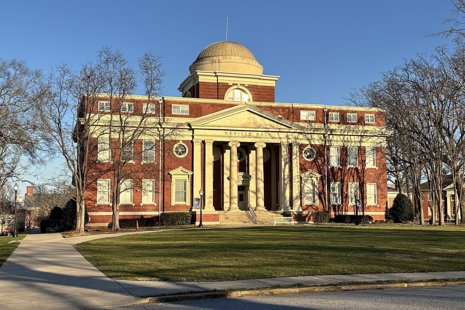 Neville Hall, a red-brick building with a white-columned portico and a dome, across a lawn at Presbyterian College in late-afternoon sun
