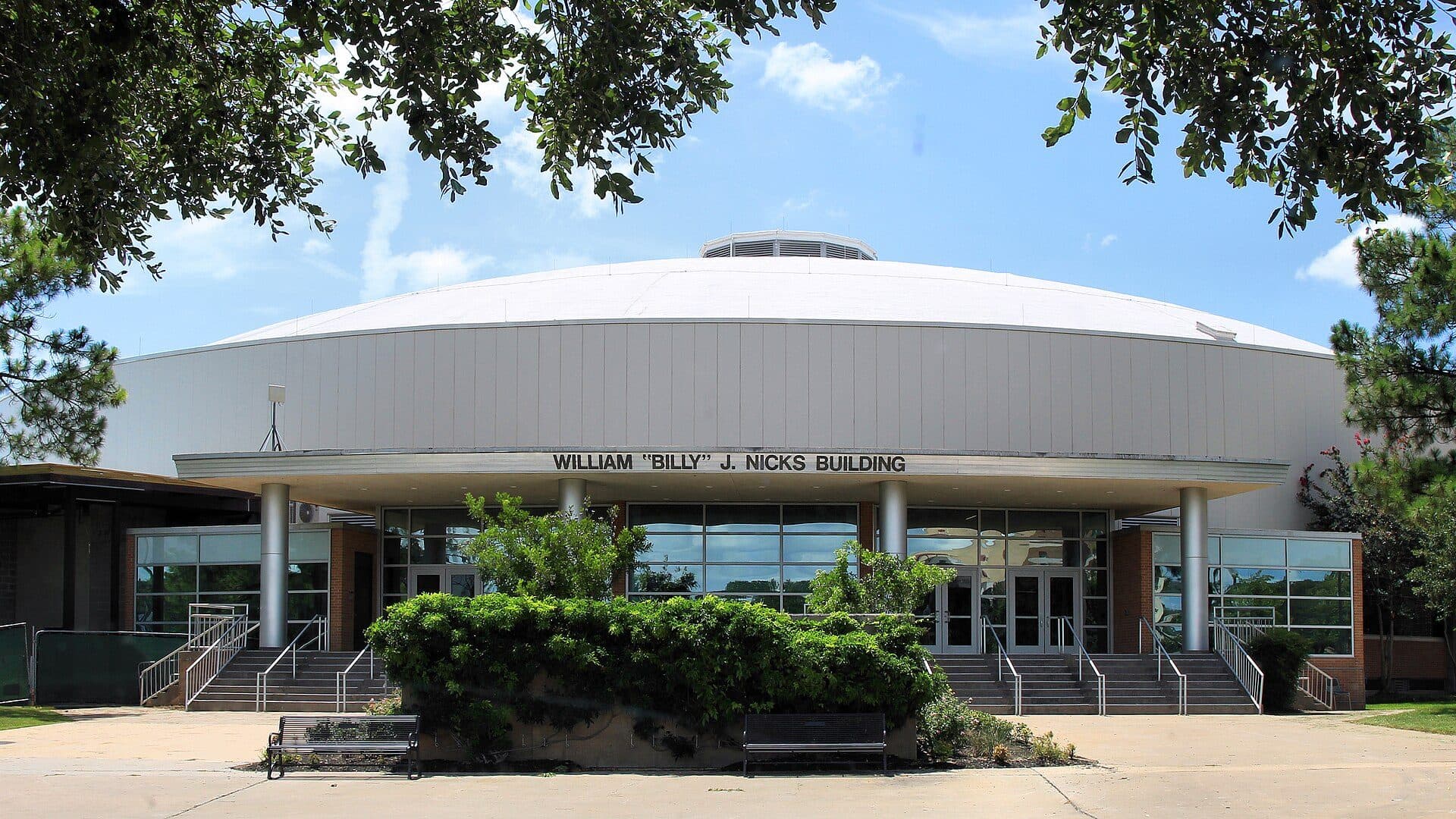 The round, domed William "Billy" J. Nicks Building at Prairie View A&M, with glass entrance doors and steps behind a hedge and benches