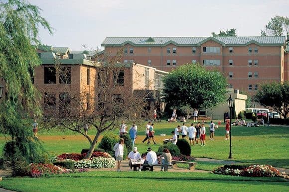 Students on a green lawn in front of brick residence halls on the Sacred Heart University campus in Fairfield
