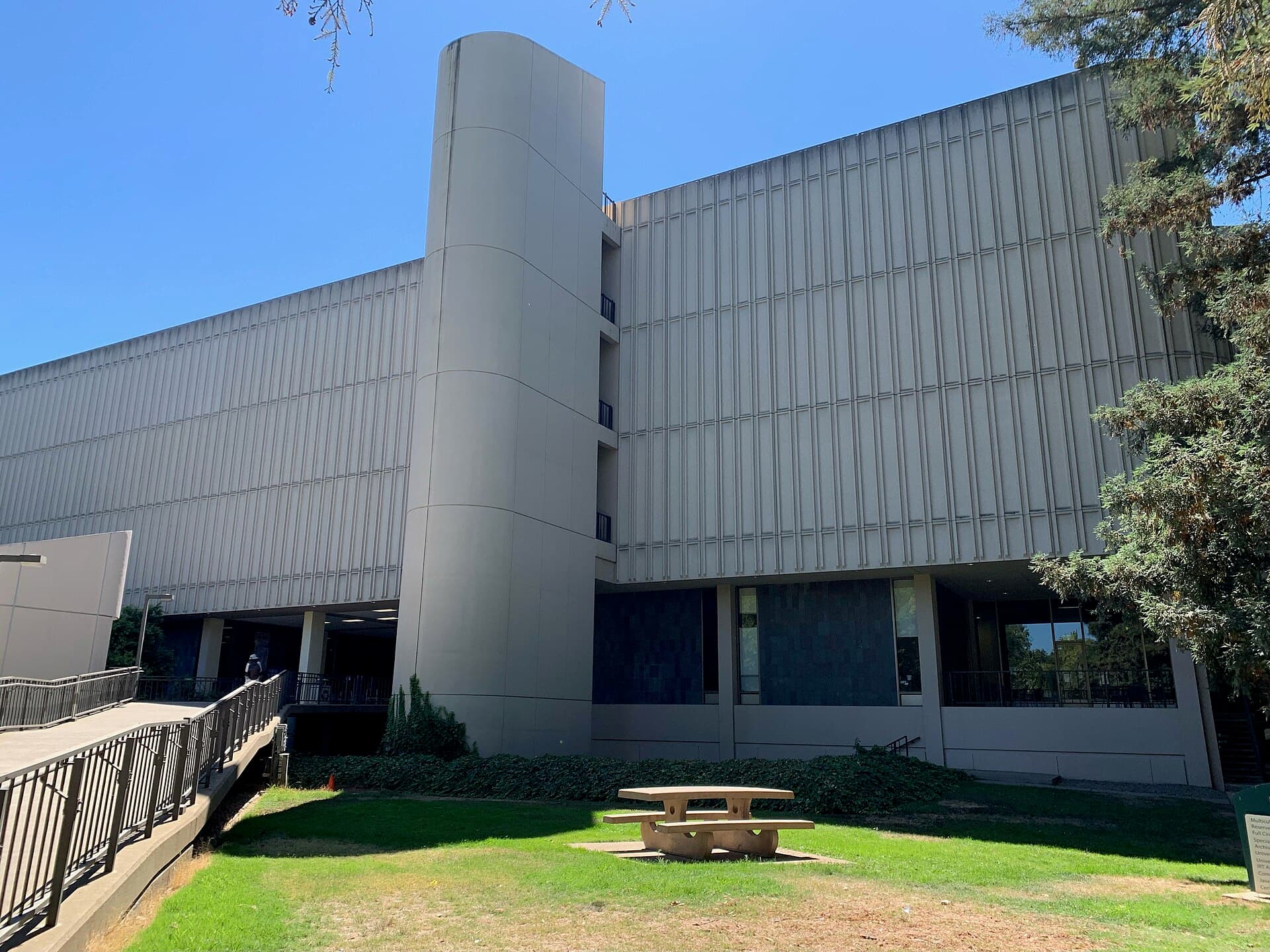 The University Library at Sacramento State, a long concrete-and-glass building with a round tower, behind a lawn with picnic tables