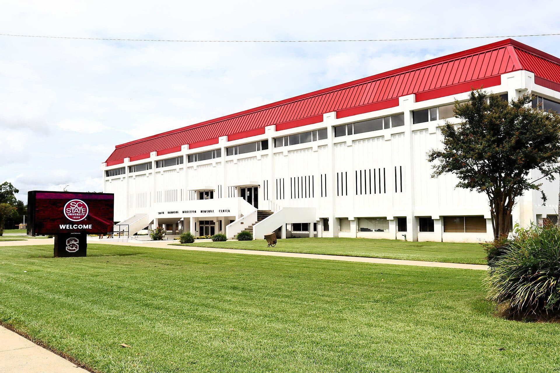 A long white arena with a red roof behind a green lawn and a welcome sign at South Carolina State University