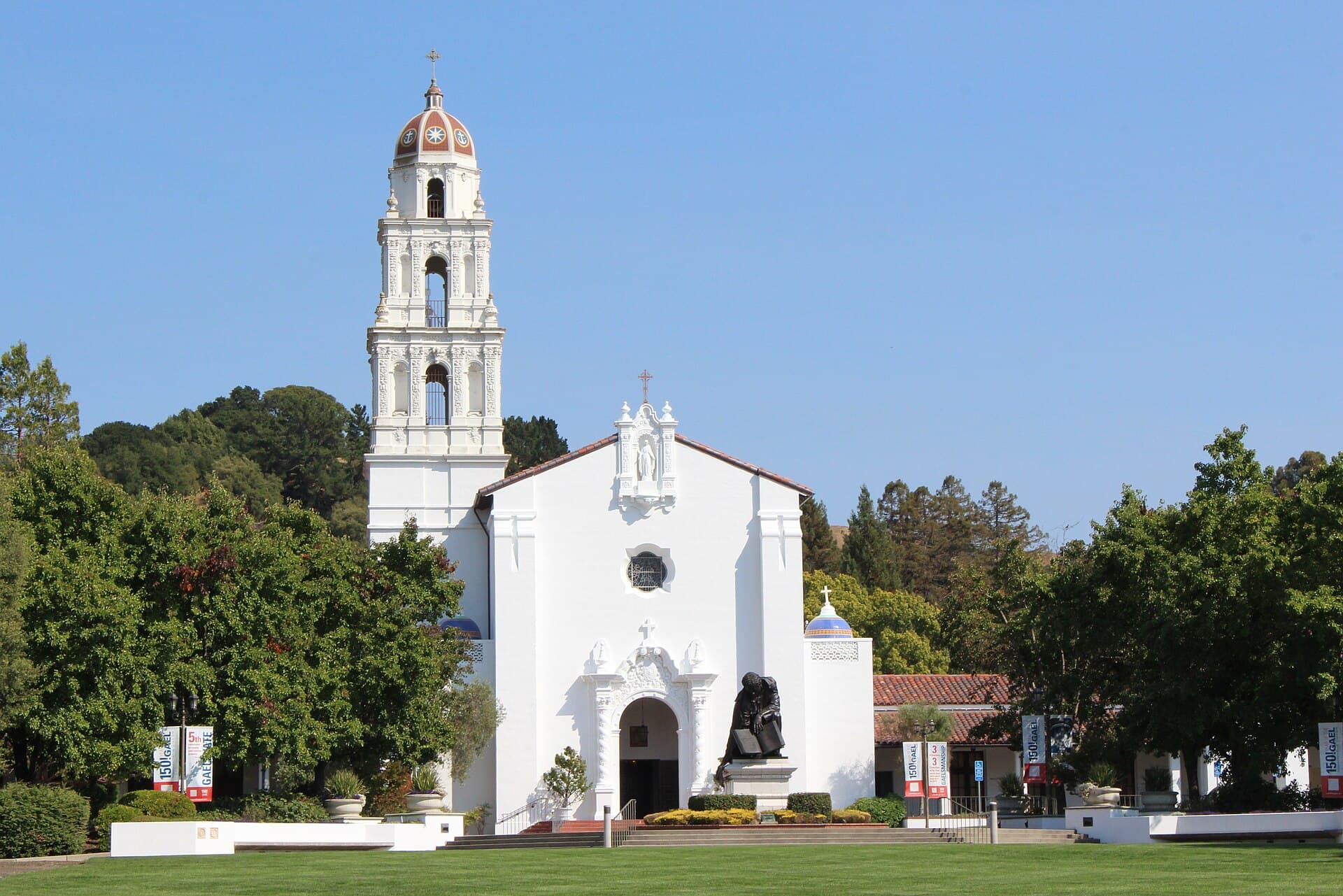 The white Mission-style chapel at Saint Mary's College with its bell tower, framed by green lawns and oak trees