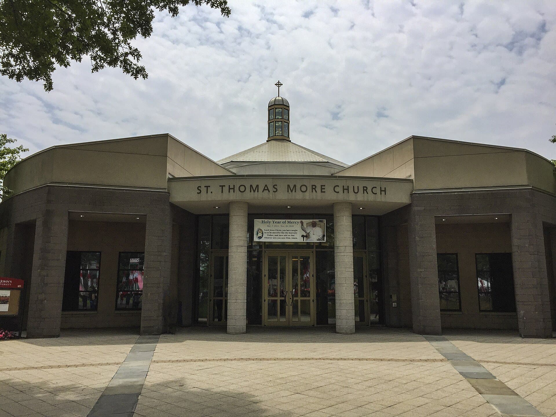 St. Thomas More Church on St. John's University's Queens campus, a low stone building with a columned entrance, its name across the front and a small cupola topped by a cross