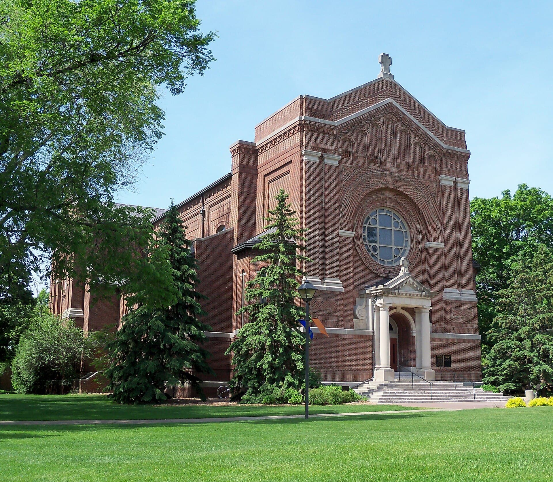 The red-brick Chapel of St. Thomas Aquinas with its round rose window and columned entrance, framed by evergreens and a green lawn