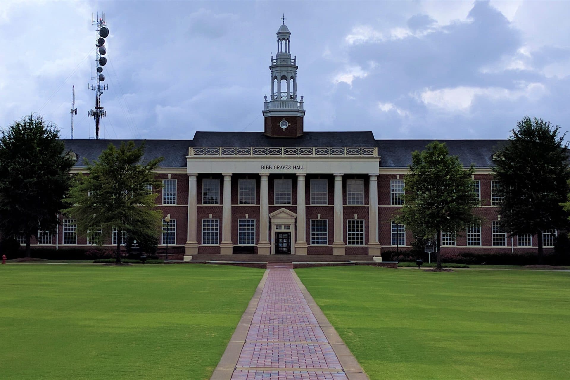 A brick walkway across a green lawn leading to Bibb Graves Hall, a red-brick building with white columns and a cupola