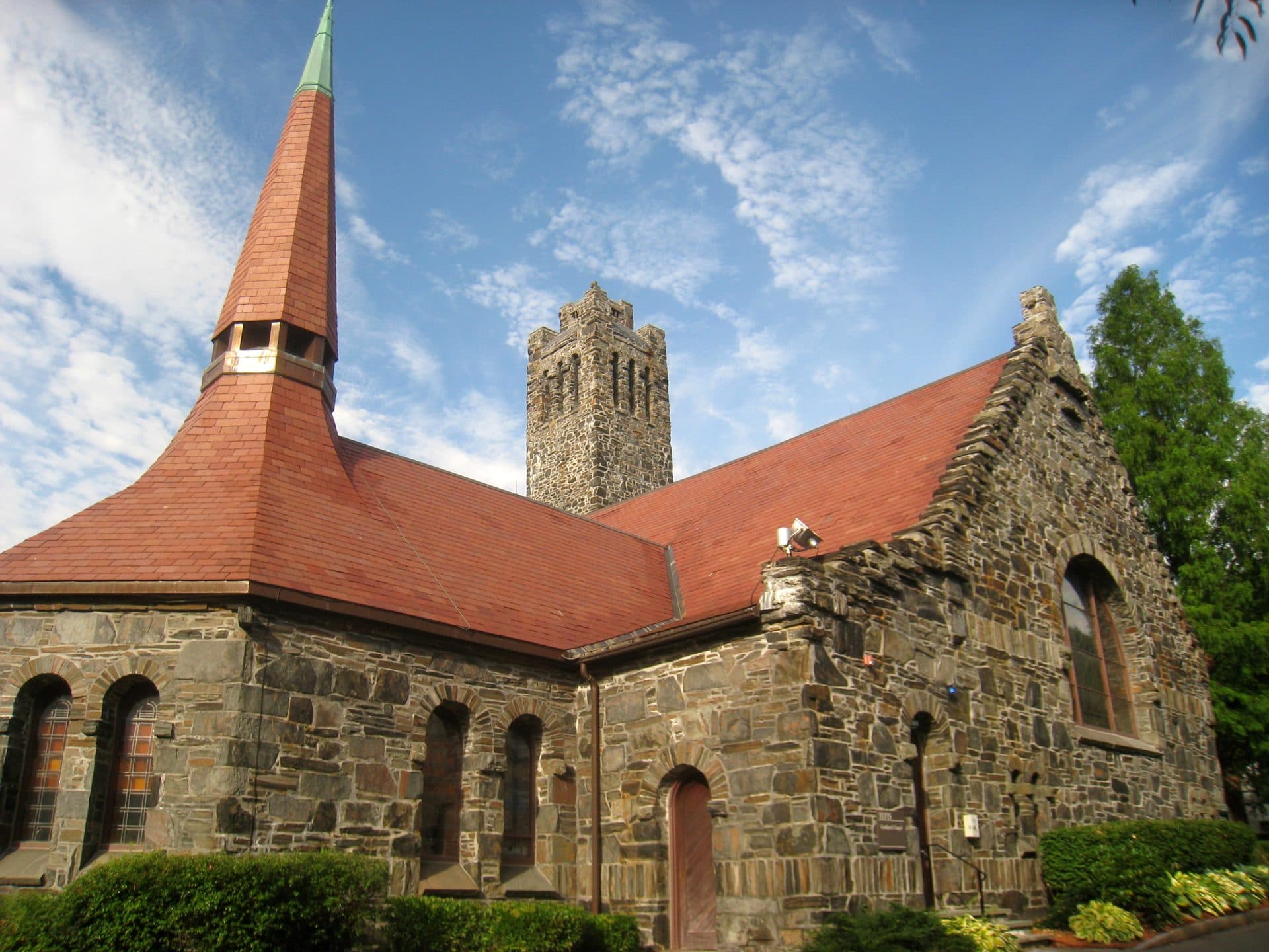 Goddard Chapel at Tufts University, a stone chapel with a red tile roof, a slender spire and a square bell tower, under a blue sky