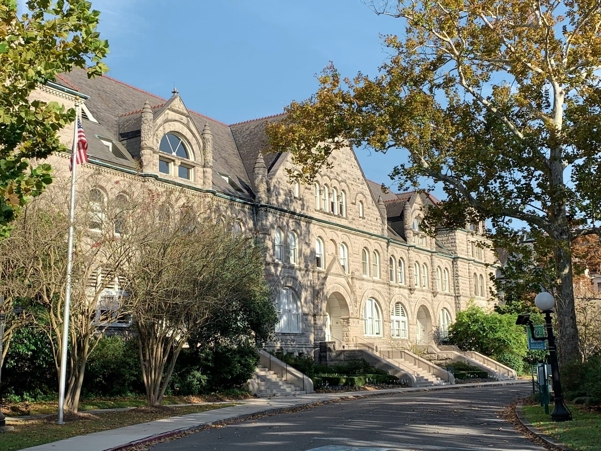 Gibson Hall at Tulane, a long pale stone Romanesque building with arched windows and front stairs, framed by trees along a curving drive