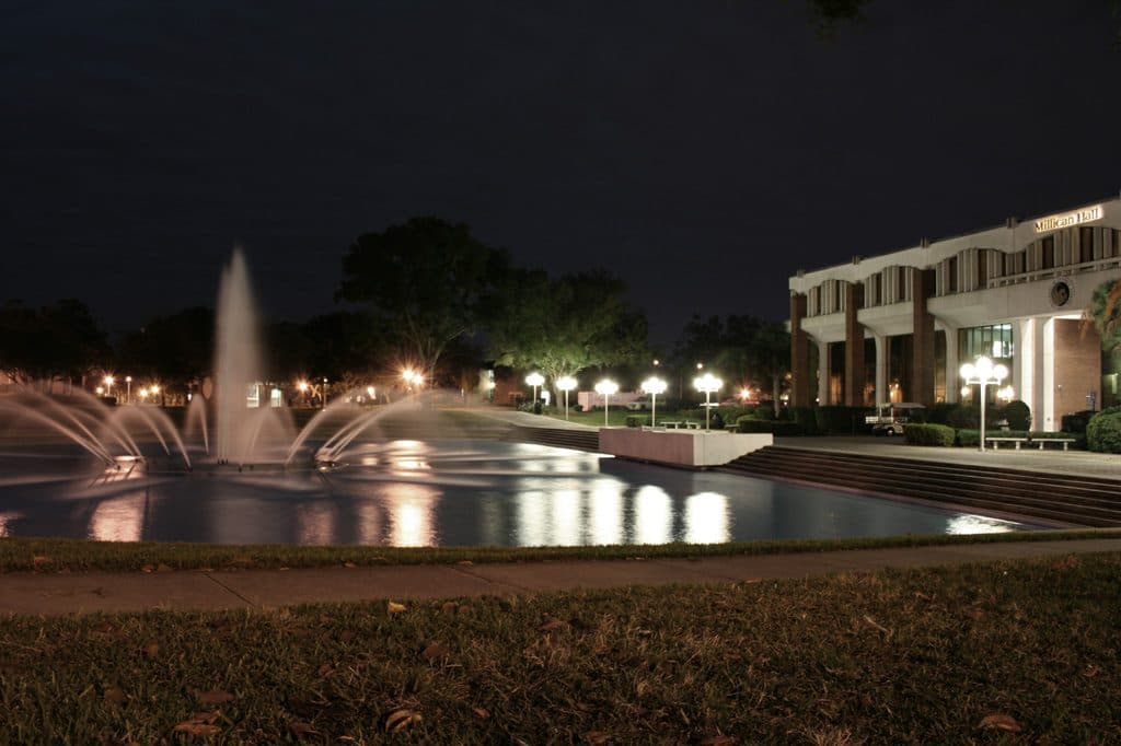 UCF's lit fountain in the Reflecting Pond at night, with Millican Hall behind it