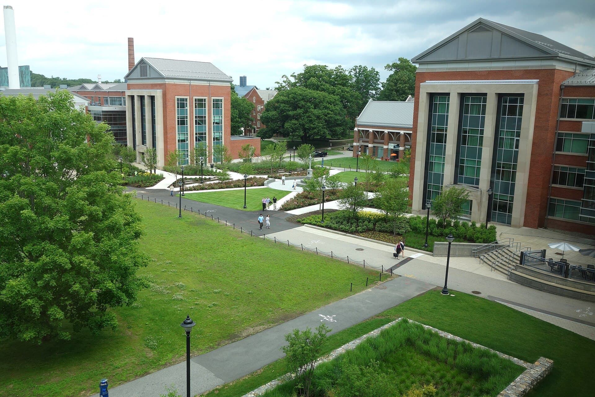 A green UConn quad in summer with lawns, paths and trees between brick academic buildings, seen from above