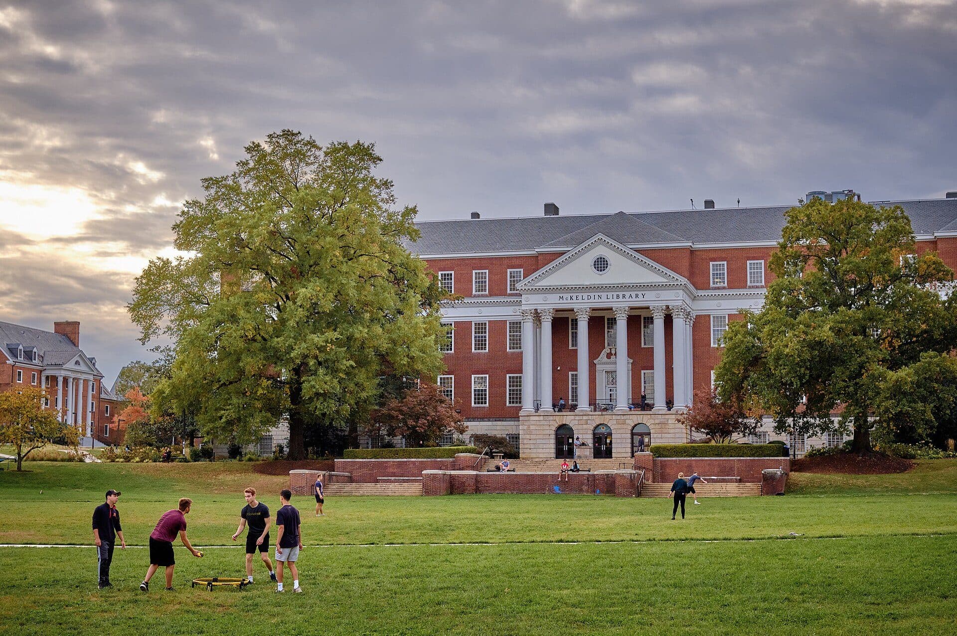 McKeldin Library's white-columned brick front at the end of McKeldin Mall, with students playing on the lawn under a cloudy sky
