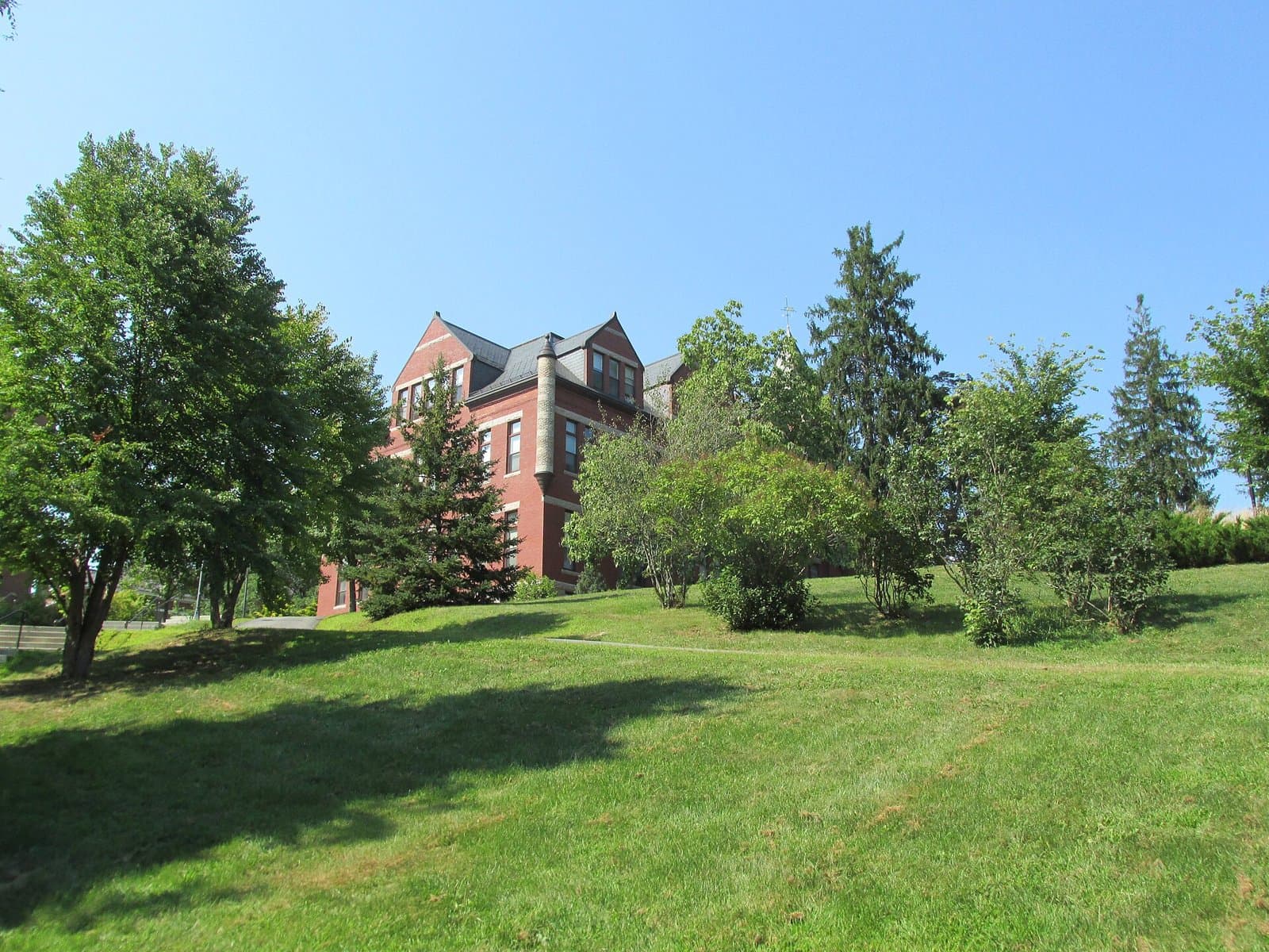 The red-brick Thompson Hall at the University of New Hampshire rising behind a grassy slope and trees under a clear summer sky