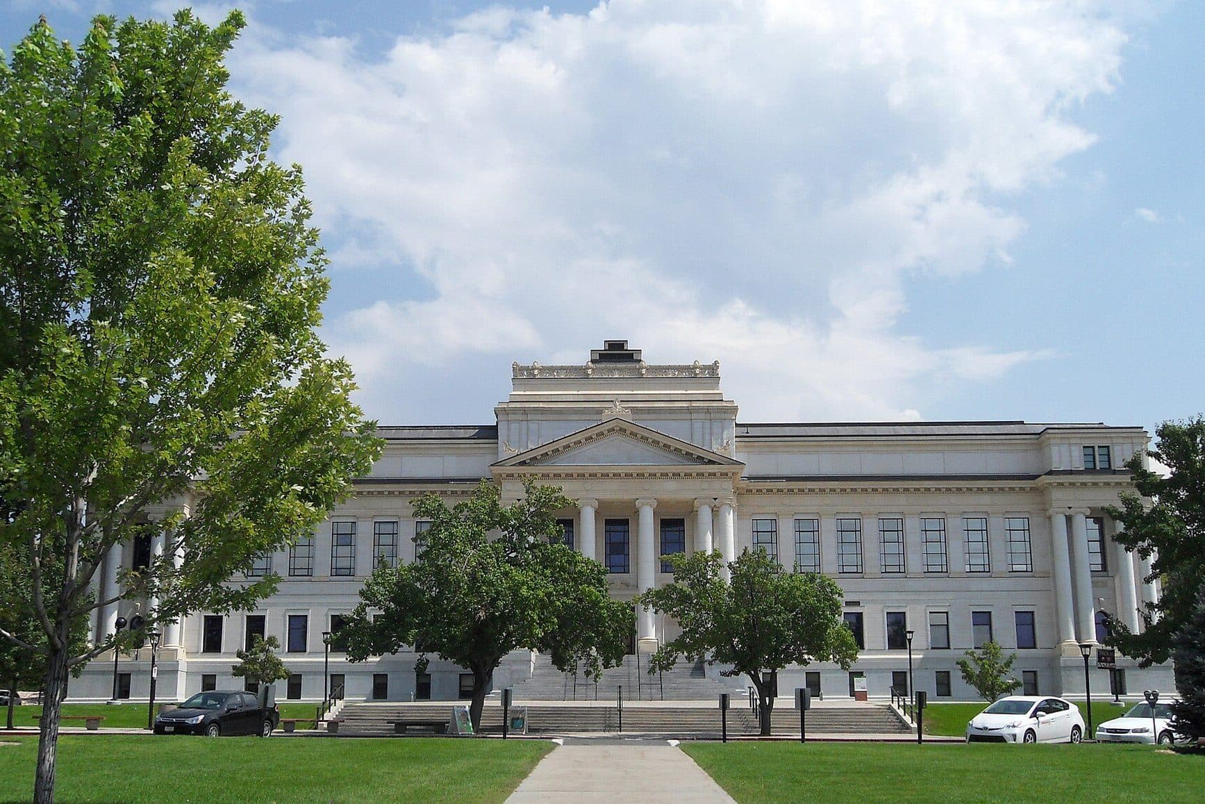 The University of Utah's columned, white Park Building at the end of a long lawn under a blue sky
