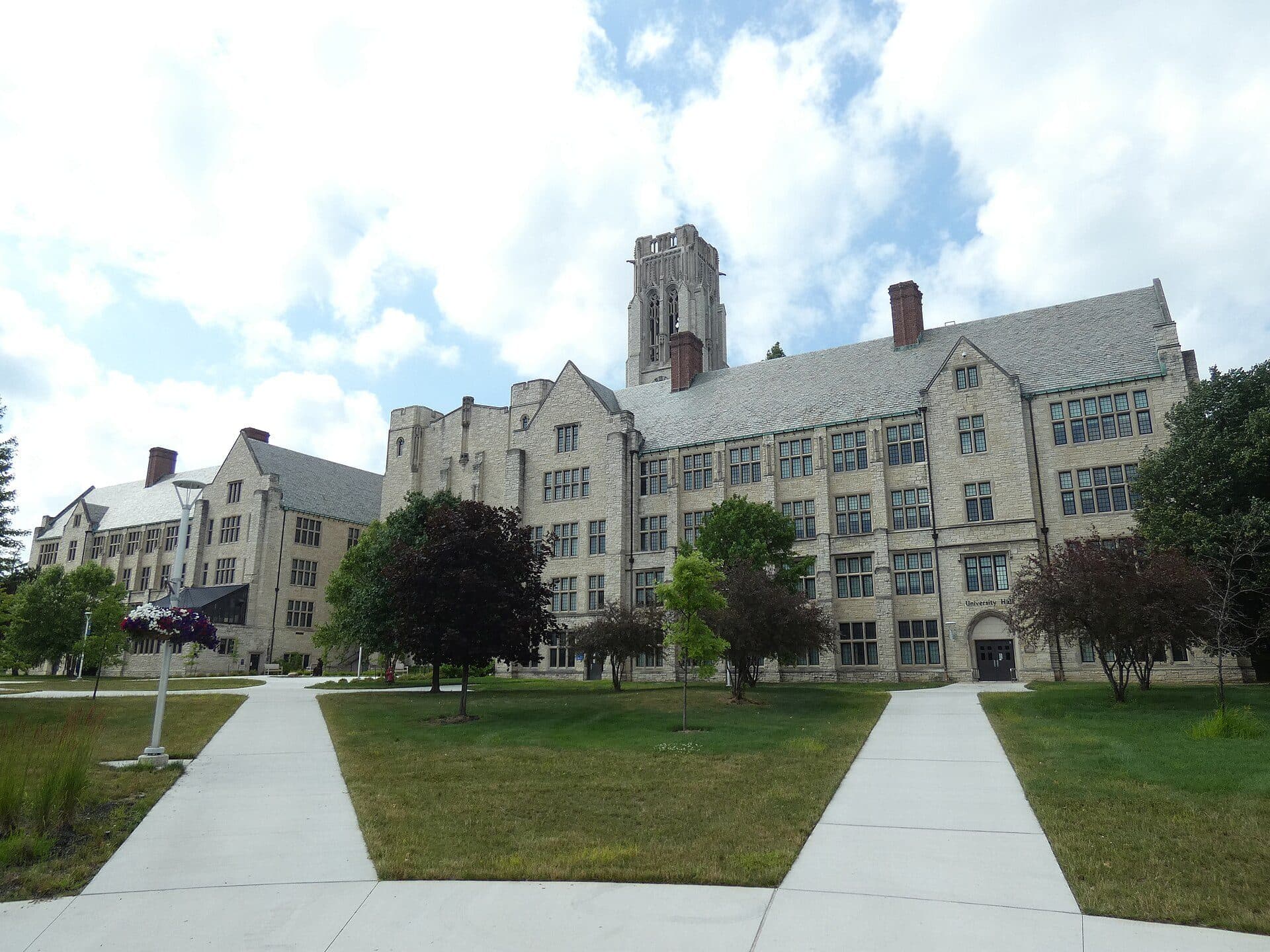 The Gothic-style stone University Hall at the University of Toledo with its central clock tower, seen from a curving campus walkway on a summer day