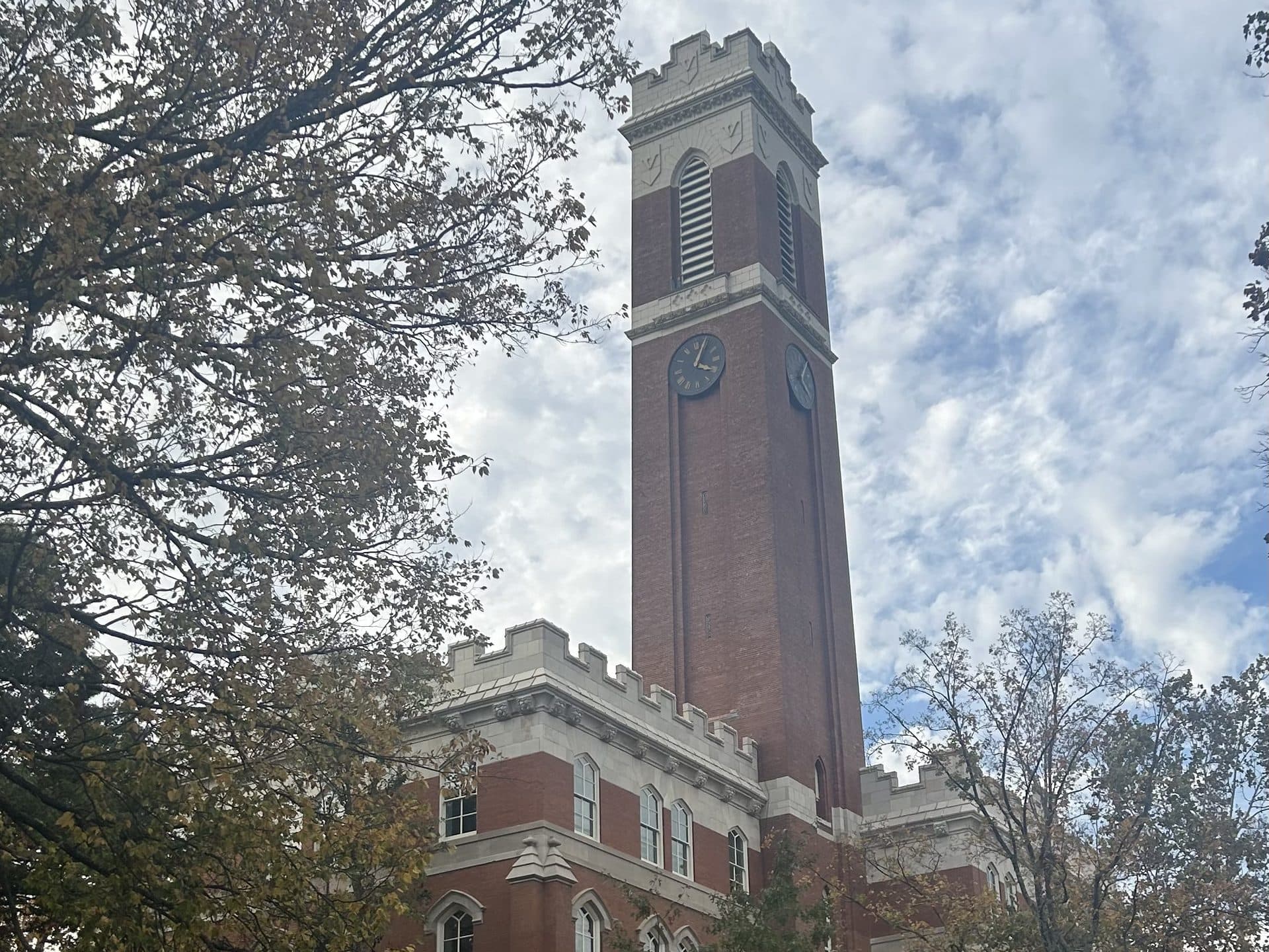 Kirkland Hall's tall red-brick clock tower with white stone trim rising above autumn trees under a cloudy sky