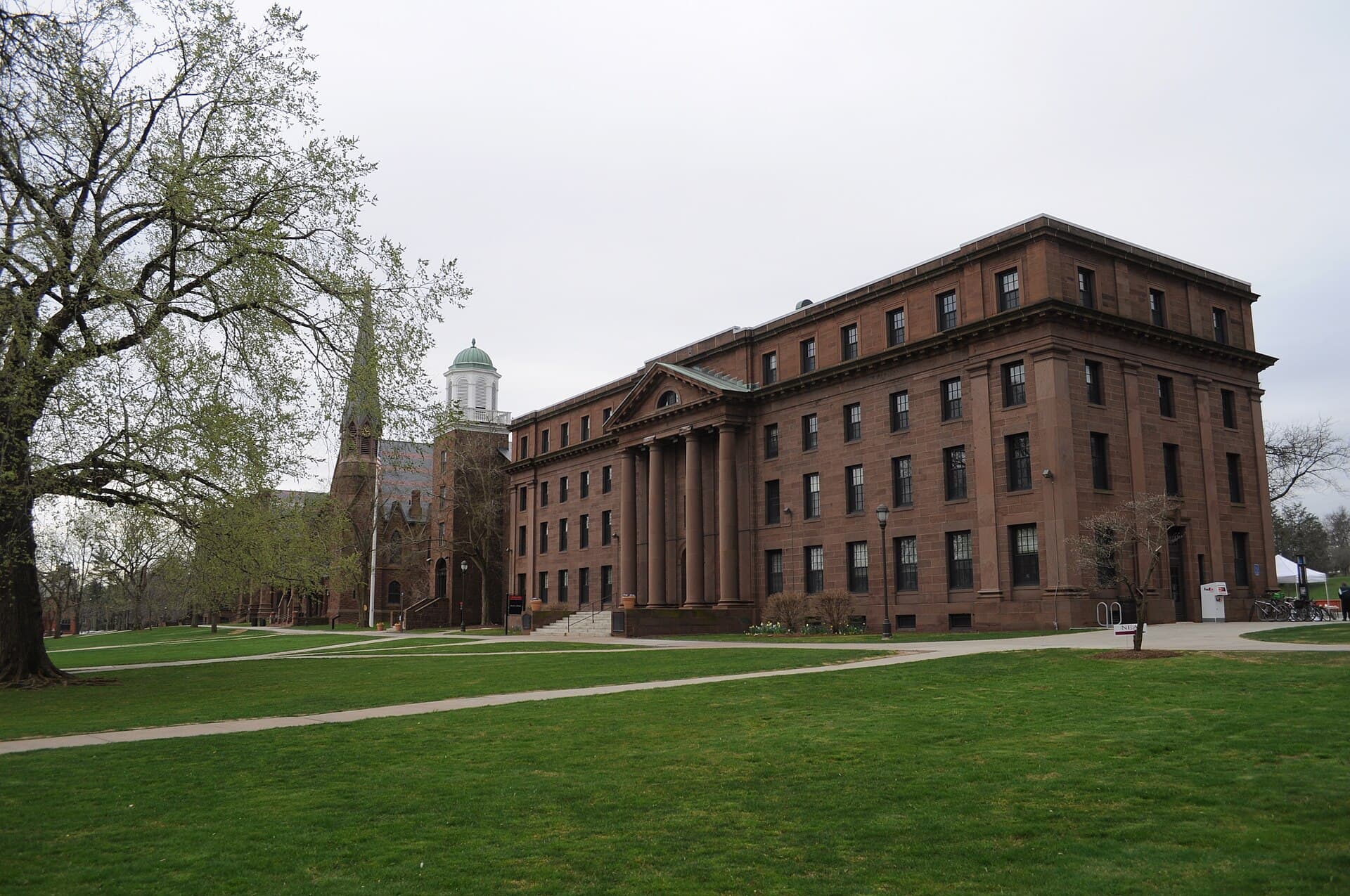 Brownstone buildings along Wesleyan's College Row, seen across a broad lawn with an early-spring tree