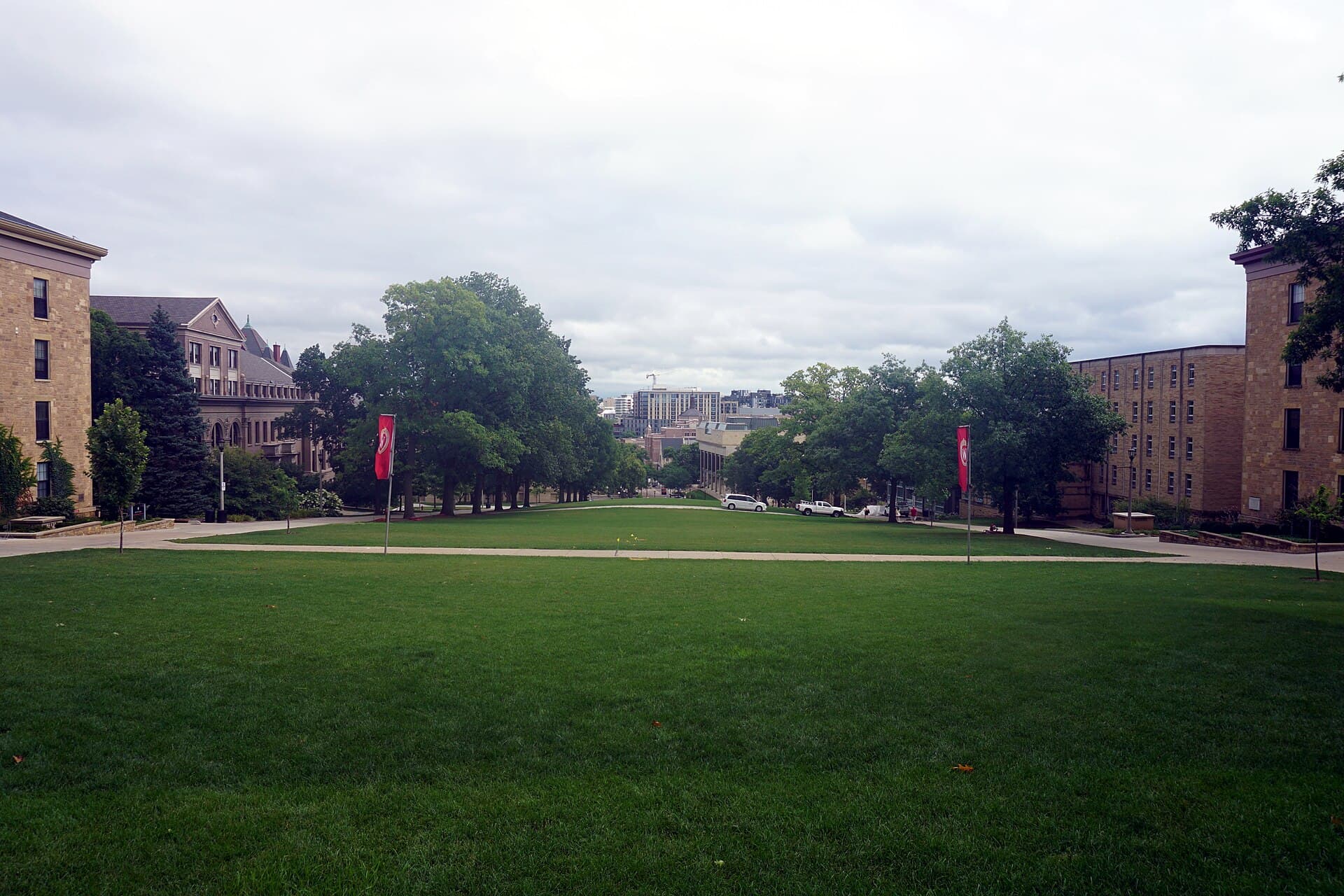 The wide lawn of Bascom Hill under an overcast sky, edged by trees and brick and stone campus buildings